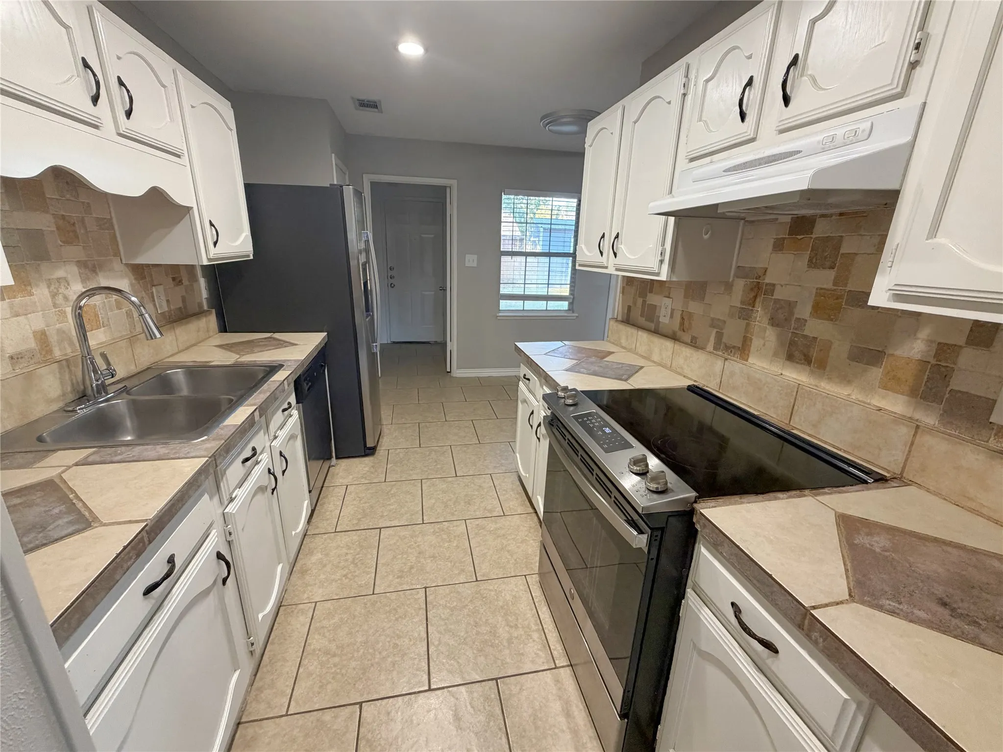 Galley kitchen featuring white cabinetry, tile countertops, a stainless steel sink, and a tile backsplash