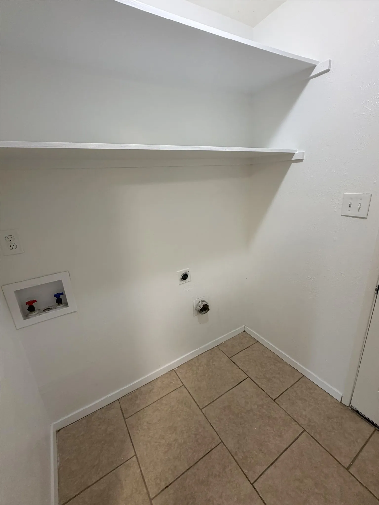 Tiled flooring with a neutral finish, built-in shelving, and dedicated utility connections