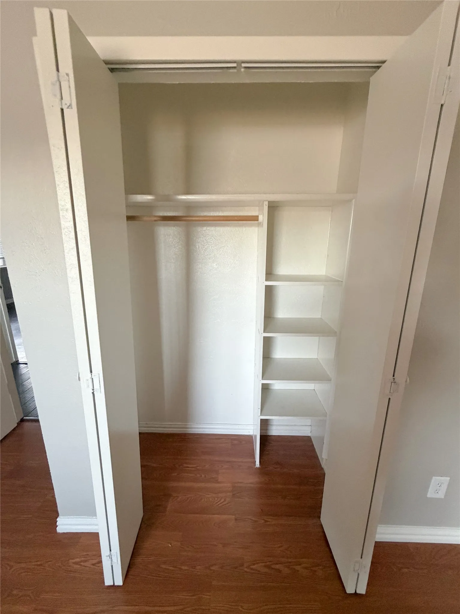 Built-in closet with wood-finish flooring, bi-fold doors, integrated shelving, and a hanging rod
