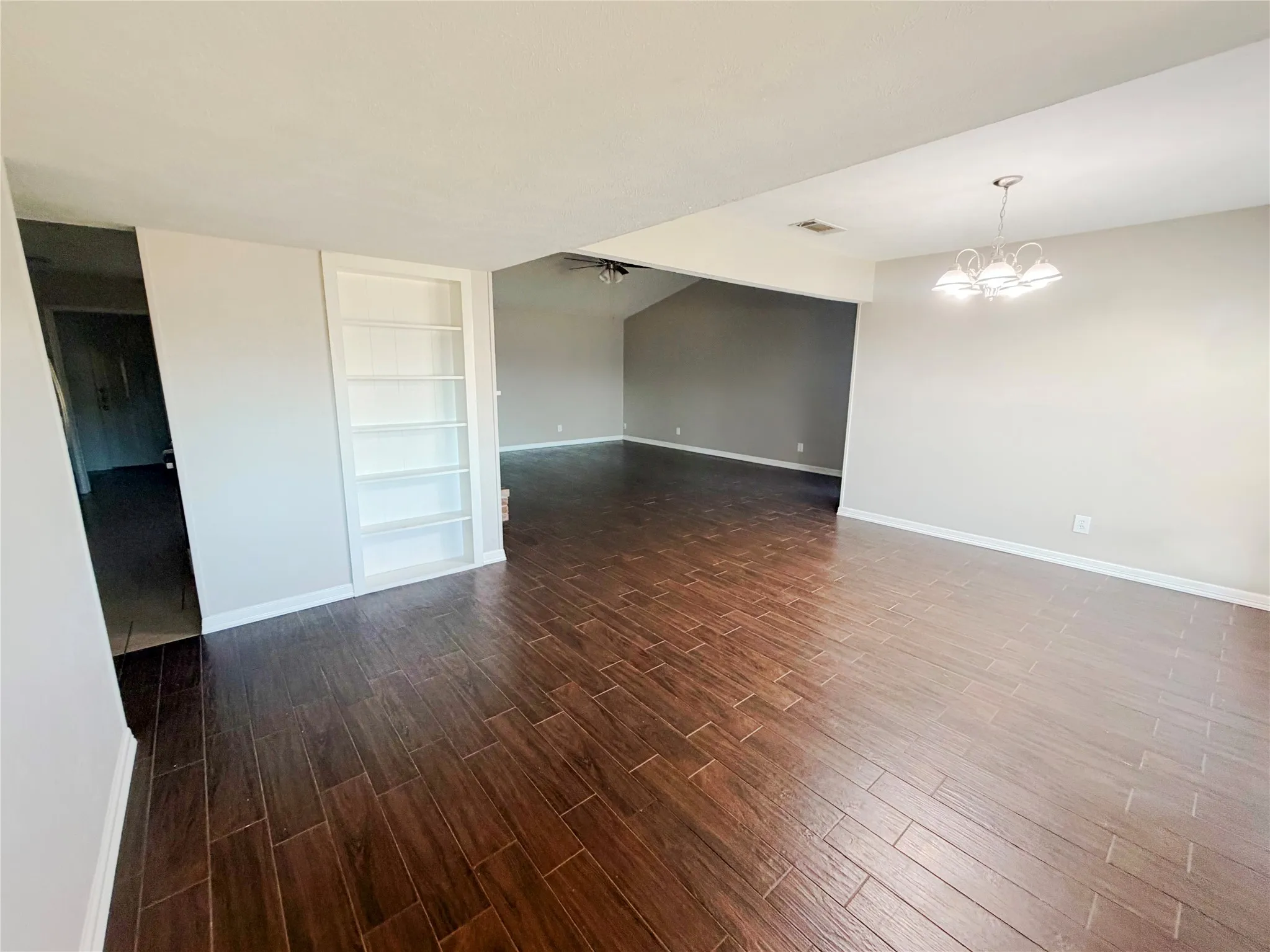 Wood-finish flooring throughout, built-in shelving, vaulted ceiling, and a chandelier with white shades
