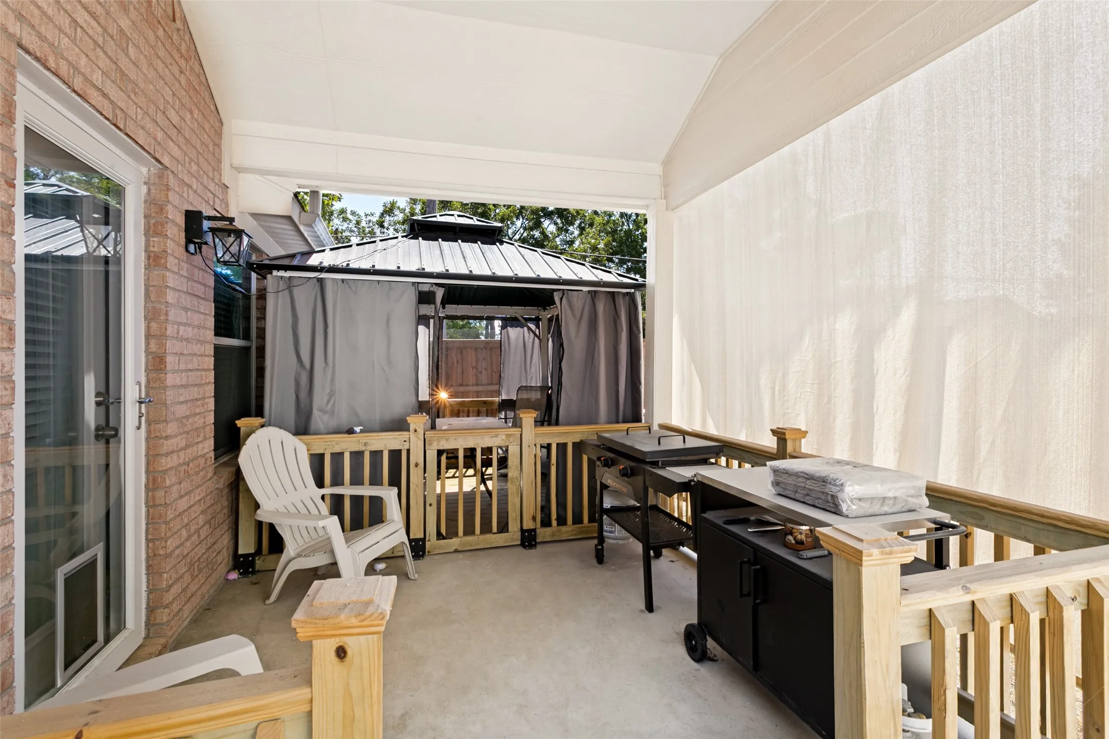 Covered patio with brick exterior, concrete flooring, and wooden railings