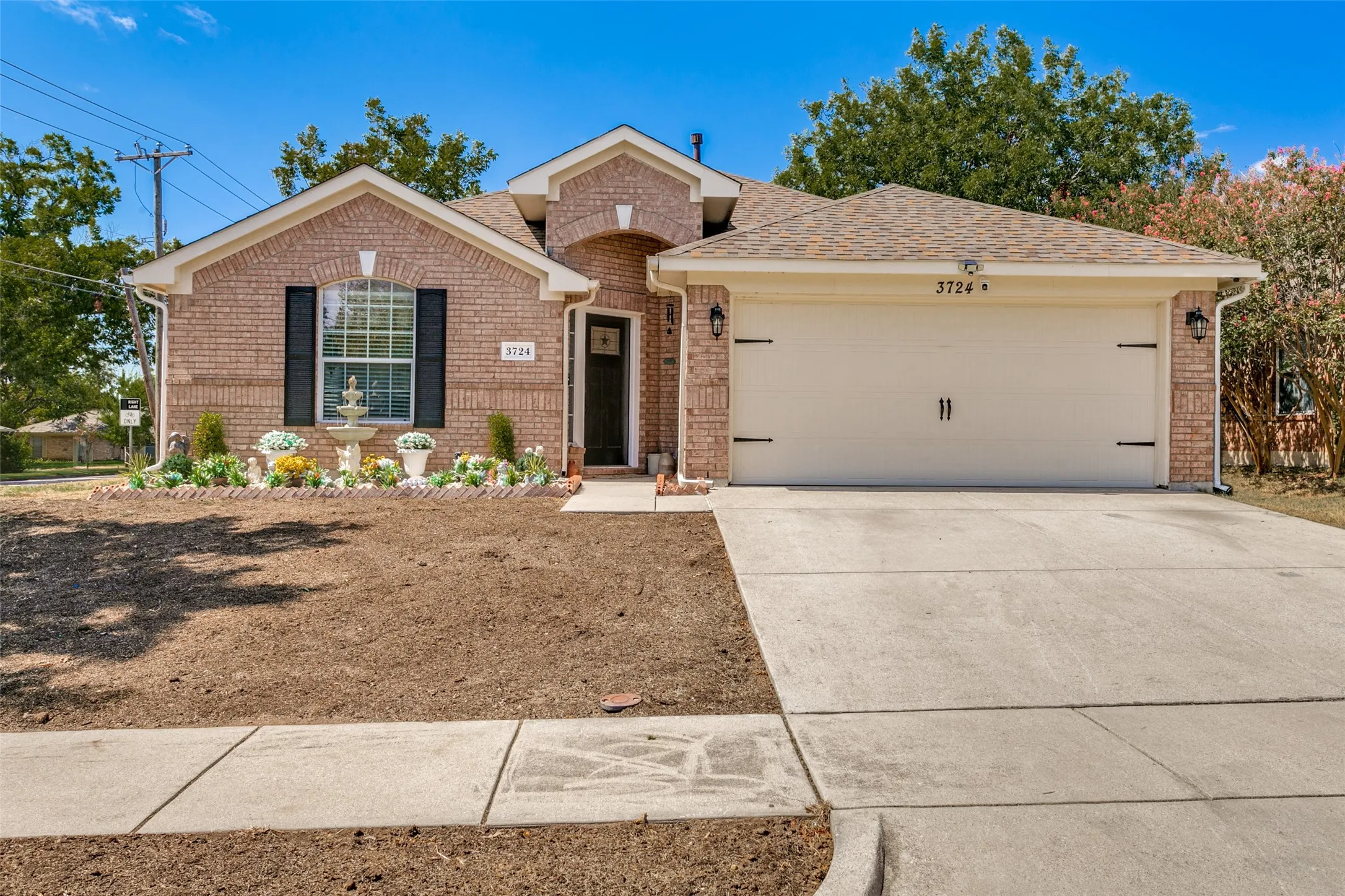 Brick-clad exterior with an arched entry, prominent front window with shutters, a concrete driveway, and an attached two-car garage