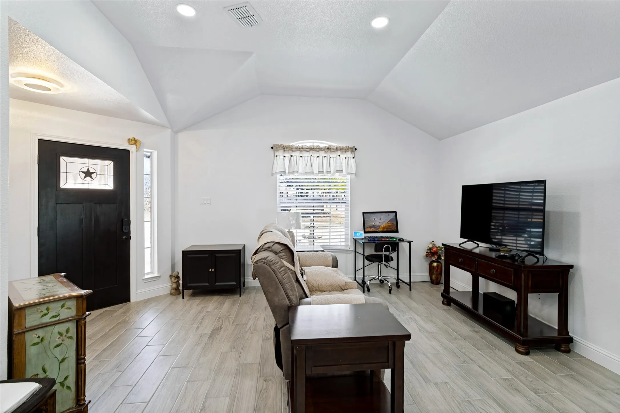 Vaulted ceiling with recessed lighting, wood-finish flooring, entry door with decorative glass insert, and a side light window