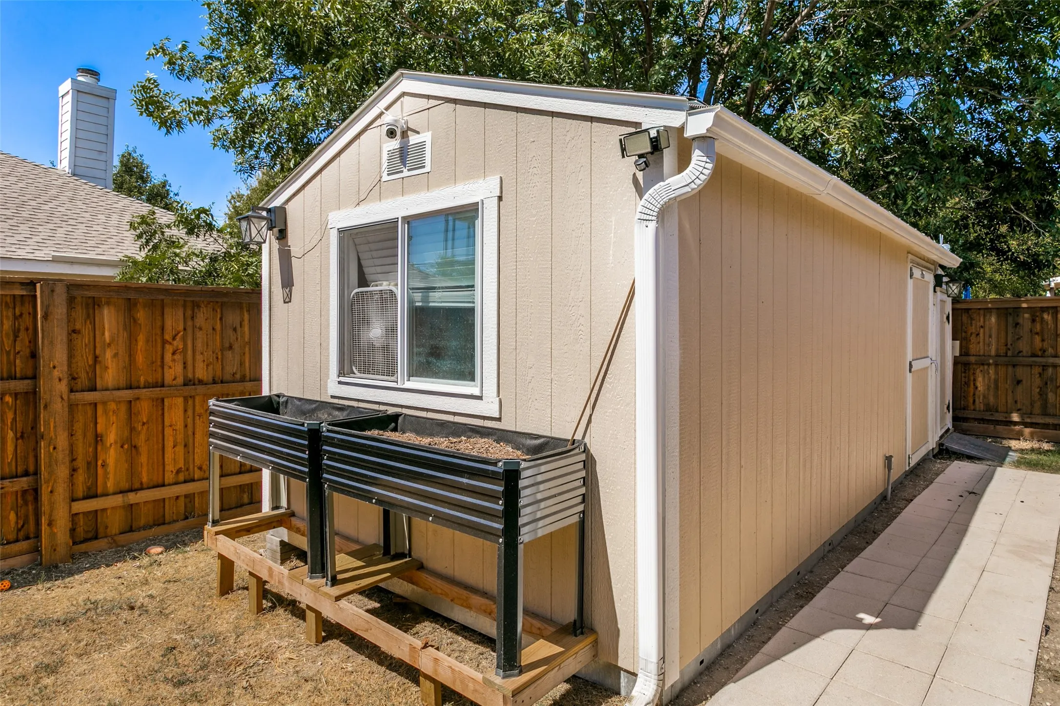 Detached structure with siding exterior and white trim, featuring a sliding window, exterior lighting, and white gutters