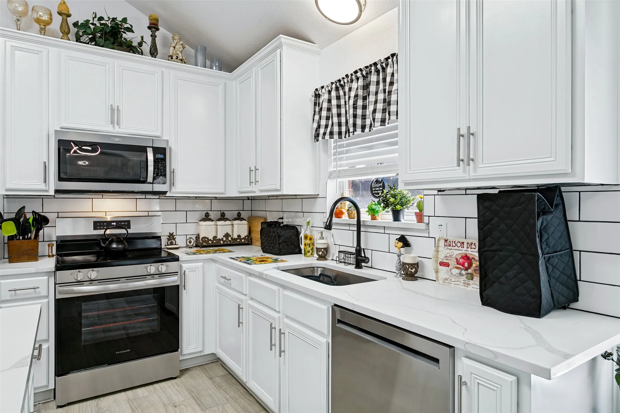 White shaker cabinetry, subway tile backsplash, stainless steel appliances, quartz countertops, and wood-finish flooring