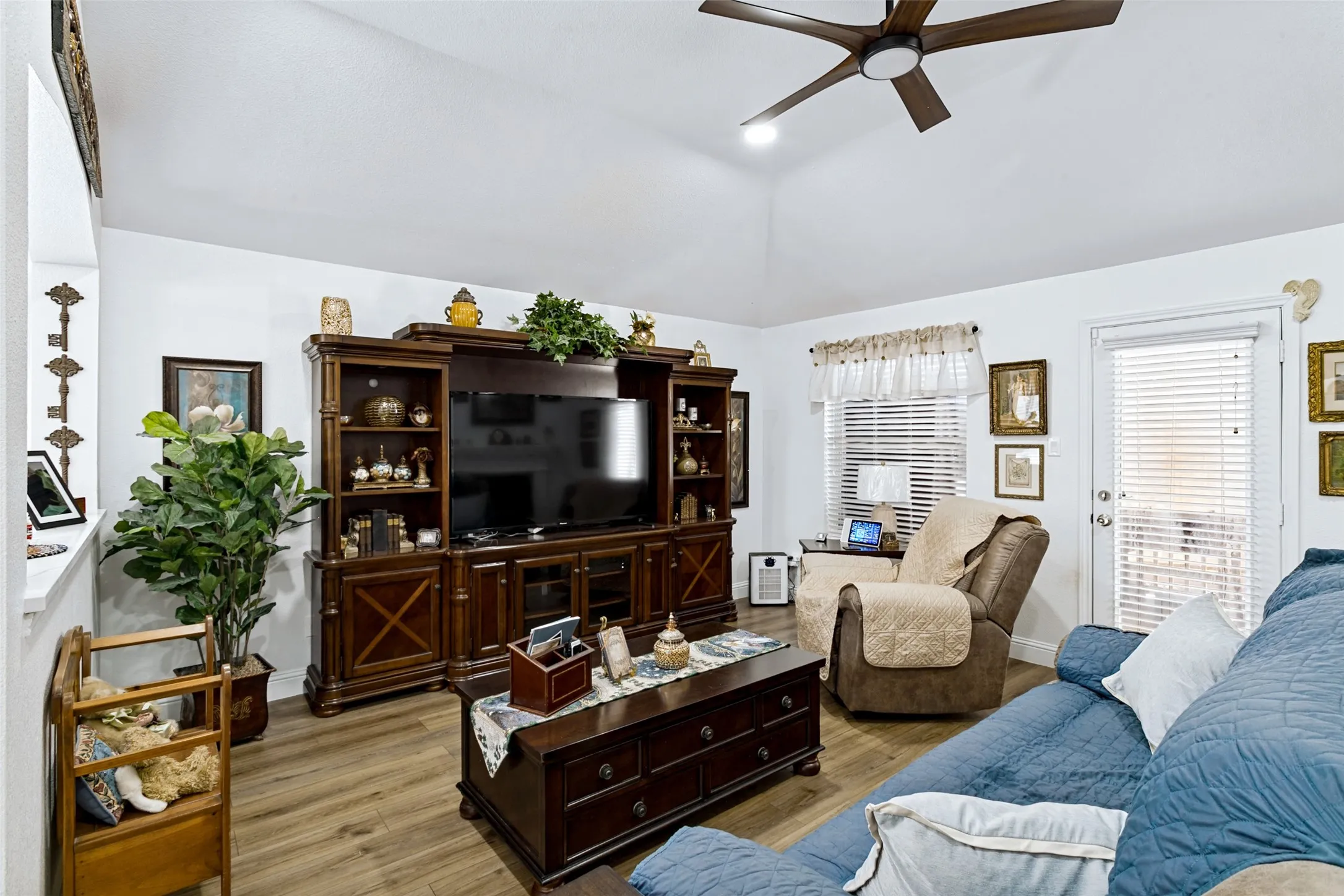 Vaulted ceiling, wood-finish flooring, ceiling fan, white walls, and a glass-paneled door