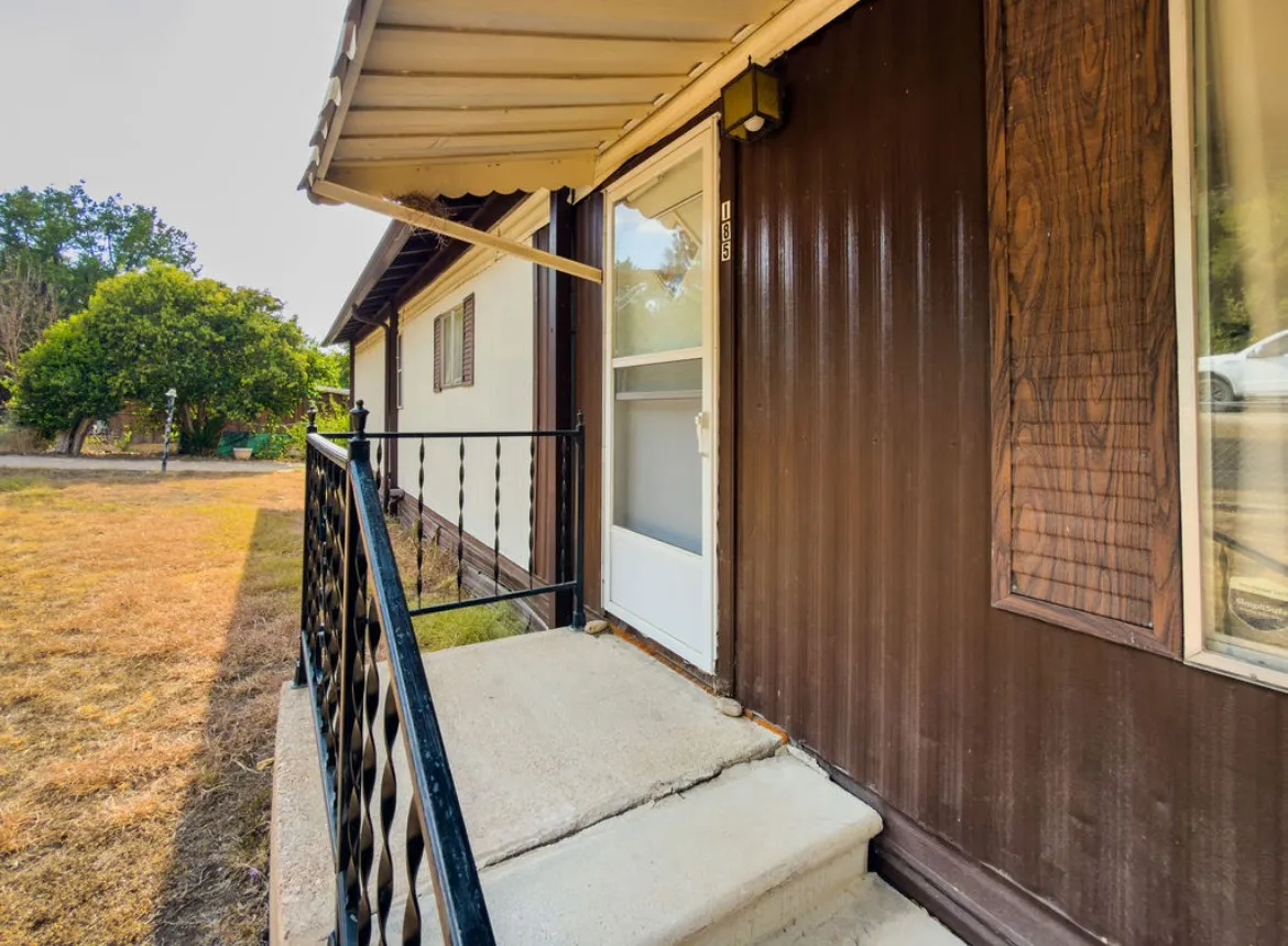 Corrugated brown siding with white trim, a concrete entry porch with black metal railings, and a white storm door