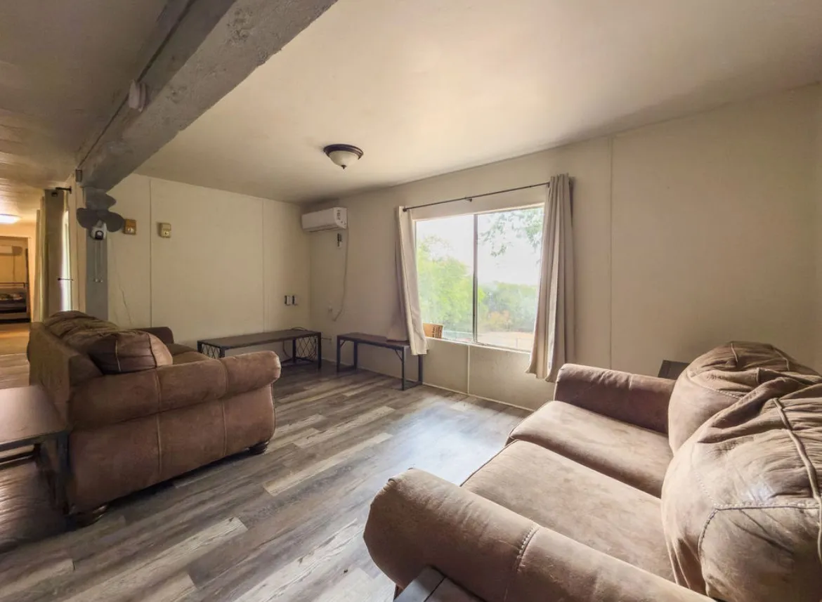 Wood-finish flooring, ceiling-mounted light fixture, window with drapes, and a wall-mounted air conditioning unit