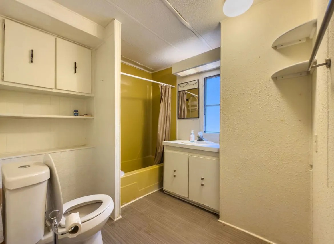 Bathroom featuring a built-in vanity with cabinetry, a window, a built-in bathtub with shower, and vinyl flooring