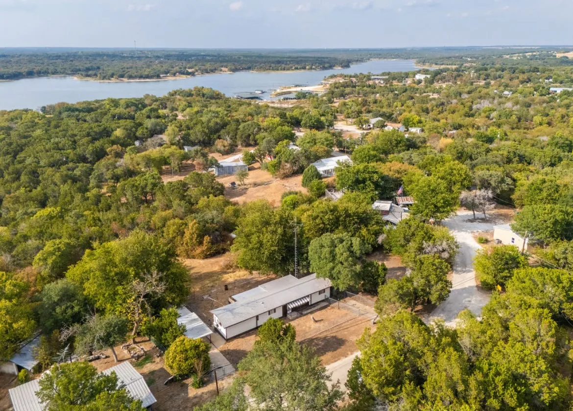 Expansive property featuring mature trees, a detached auxiliary structure, and a broad water body in the background