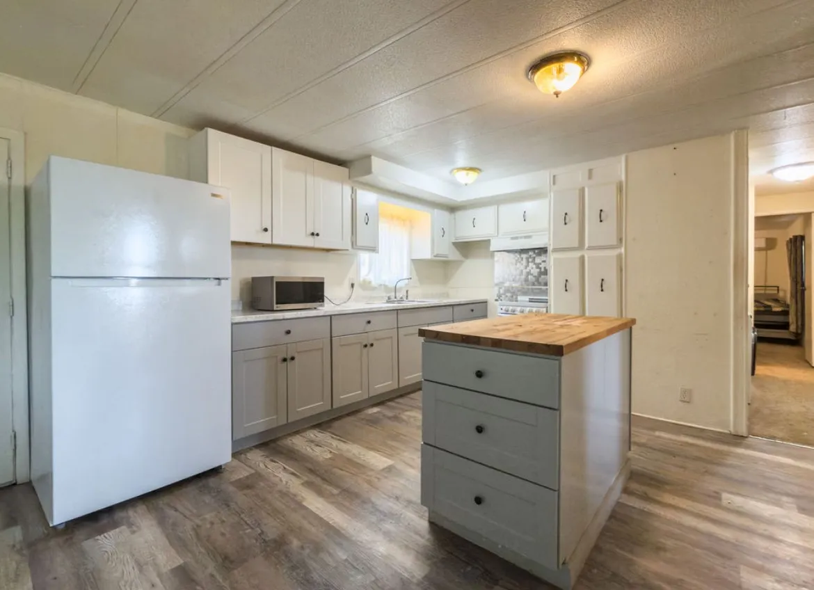 Galley kitchen featuring wood-finish flooring, two-tone cabinetry, light-toned countertops, and a central island with a wood-finish top
