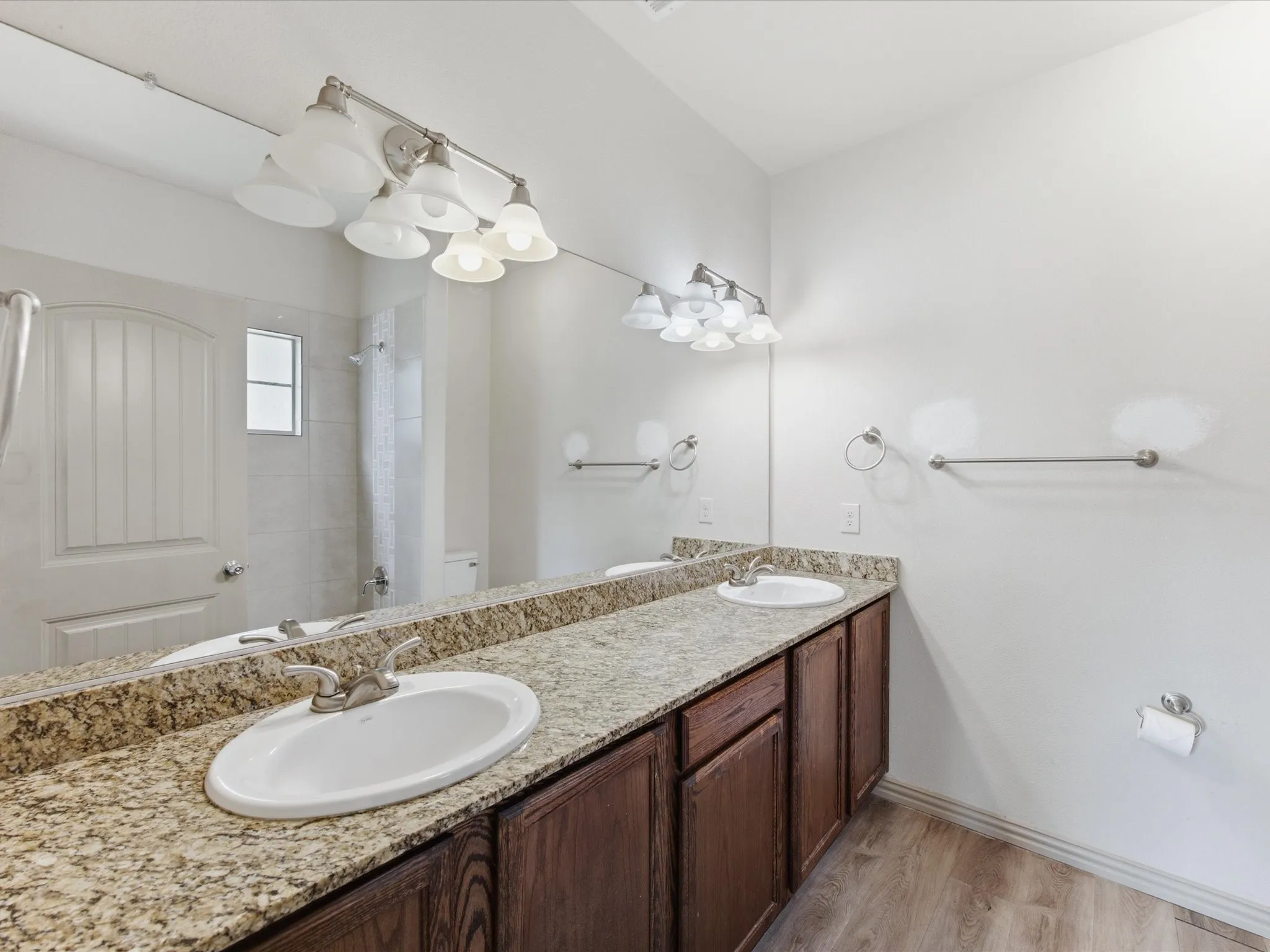 Dual vanity with granite-finish countertop, wood-finish cabinetry, and wood-finish flooring