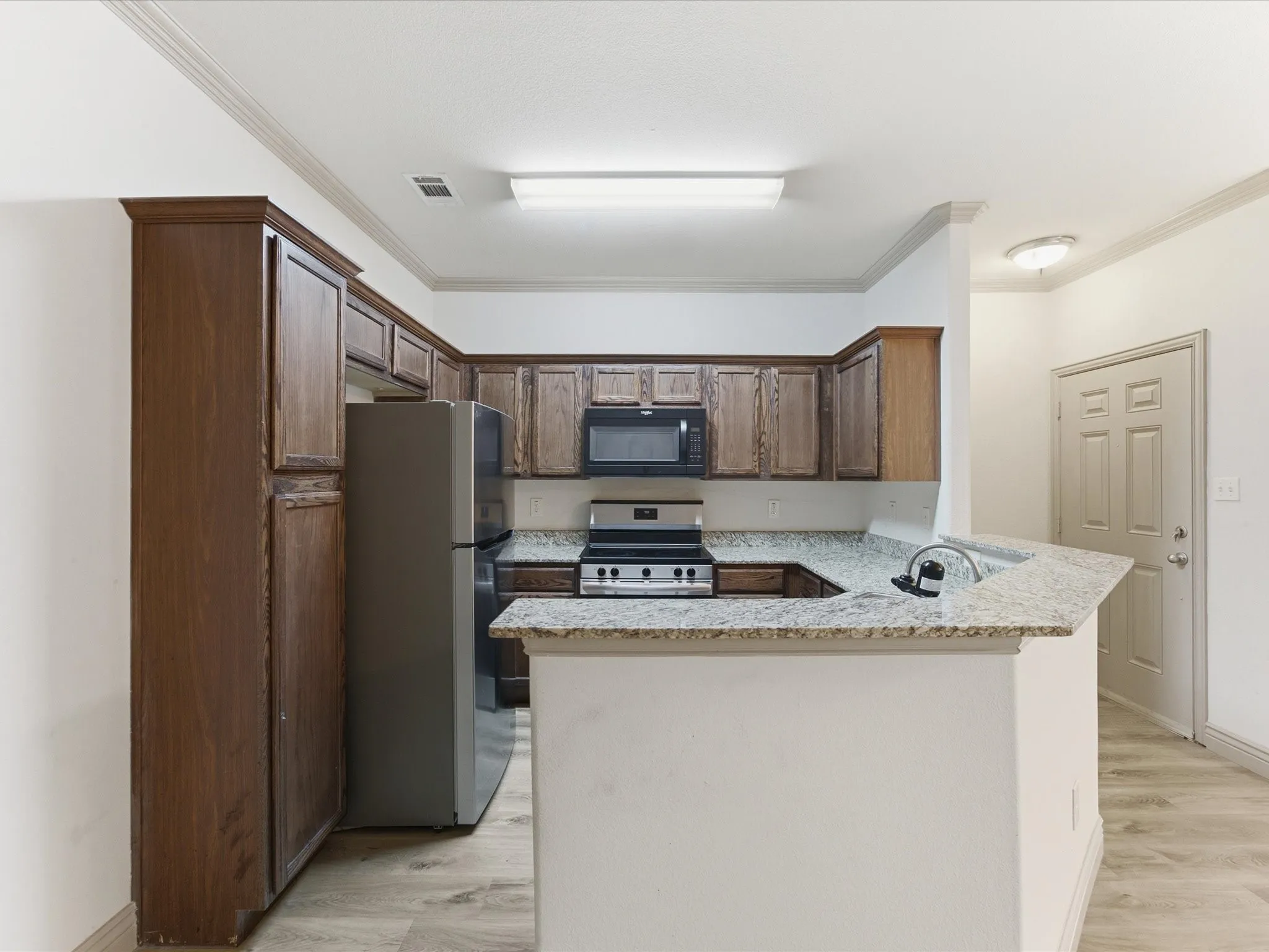 U-shaped kitchen with wood-finish cabinetry, light-toned granite countertops, and stainless steel appliances