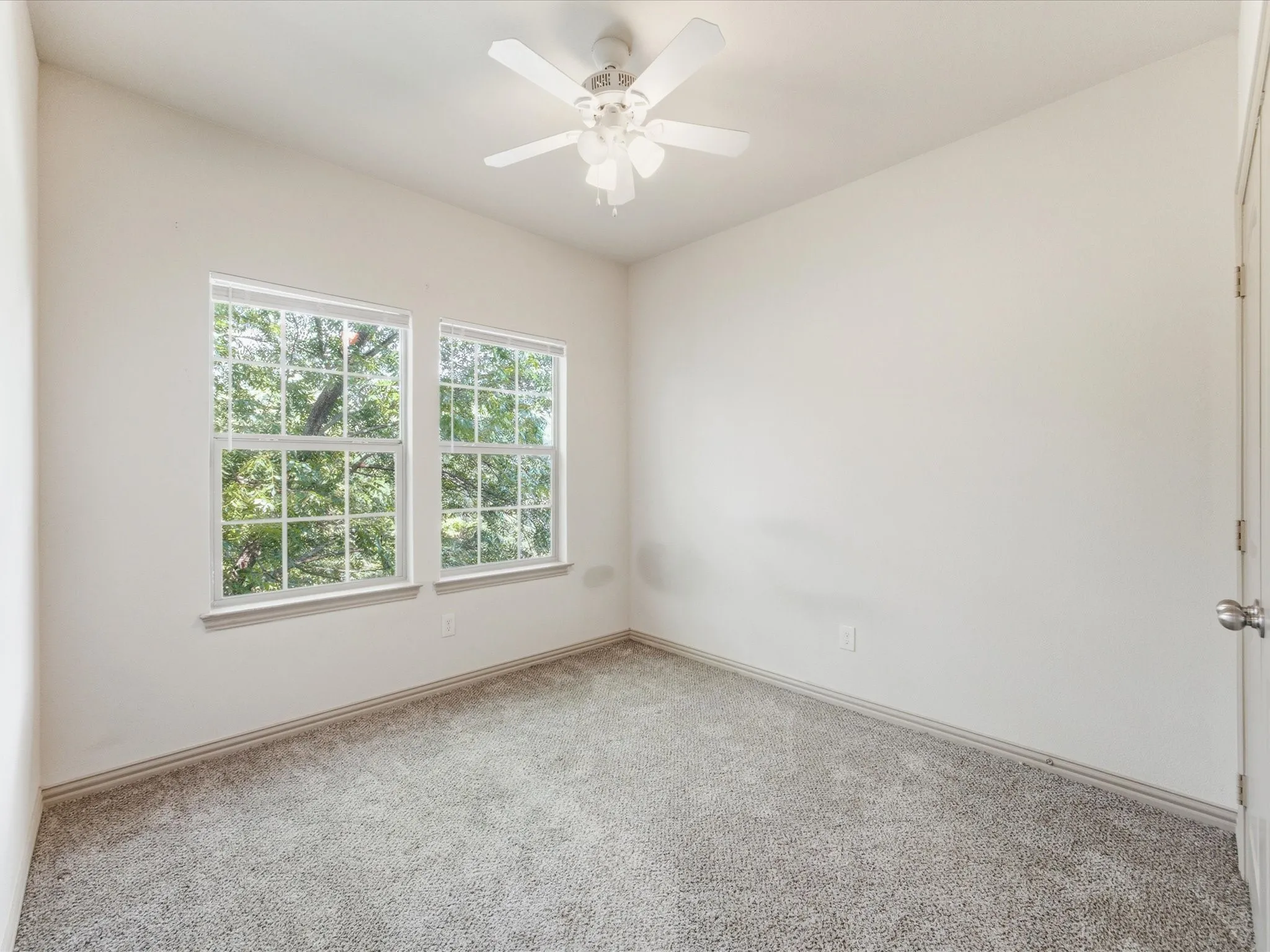 Two windows with natural light, ceiling fan, neutral wall color, and carpeted flooring