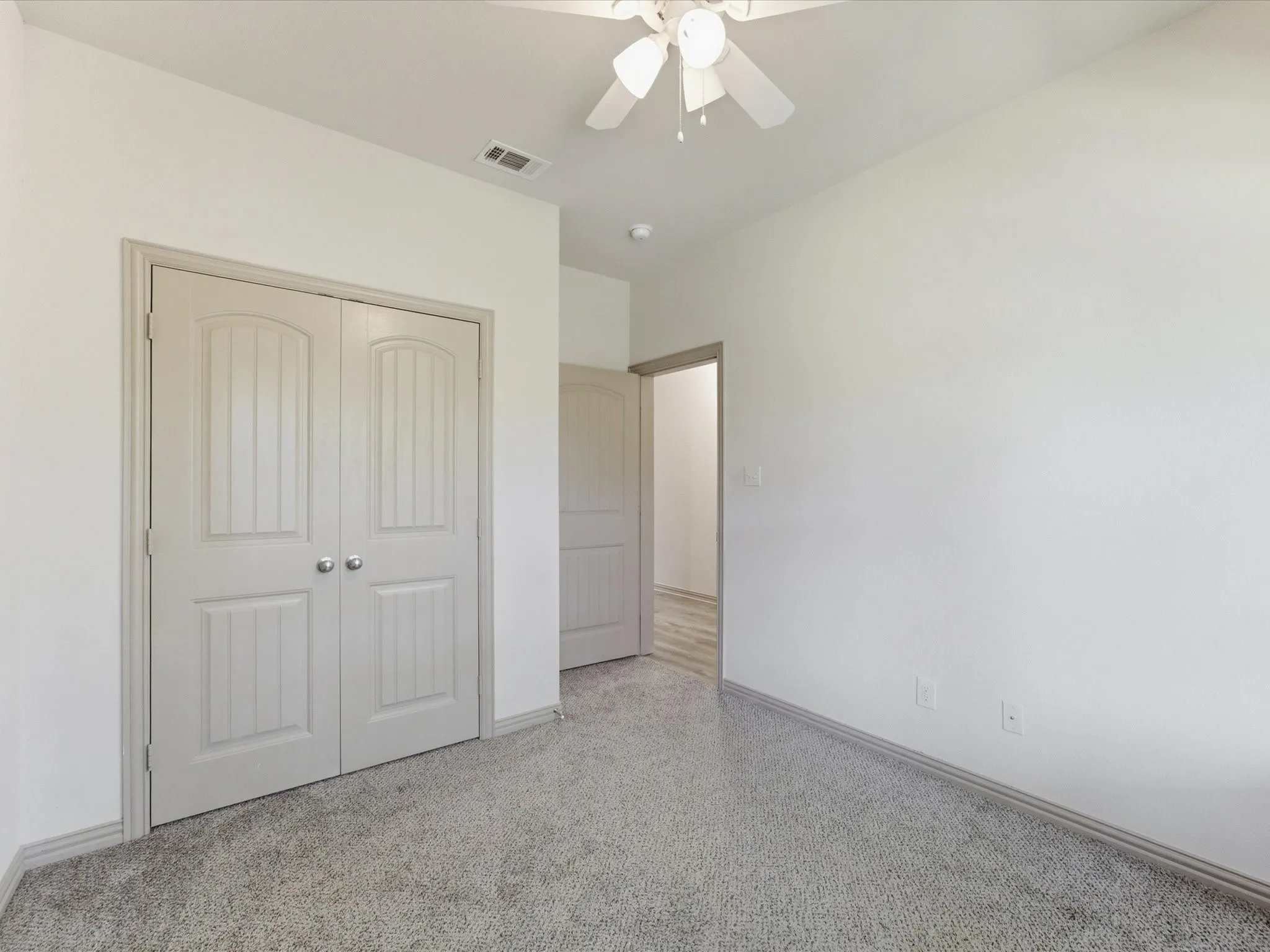 Recessed panel bi-fold closet doors, textured carpet flooring, and a ceiling fan with integrated lighting