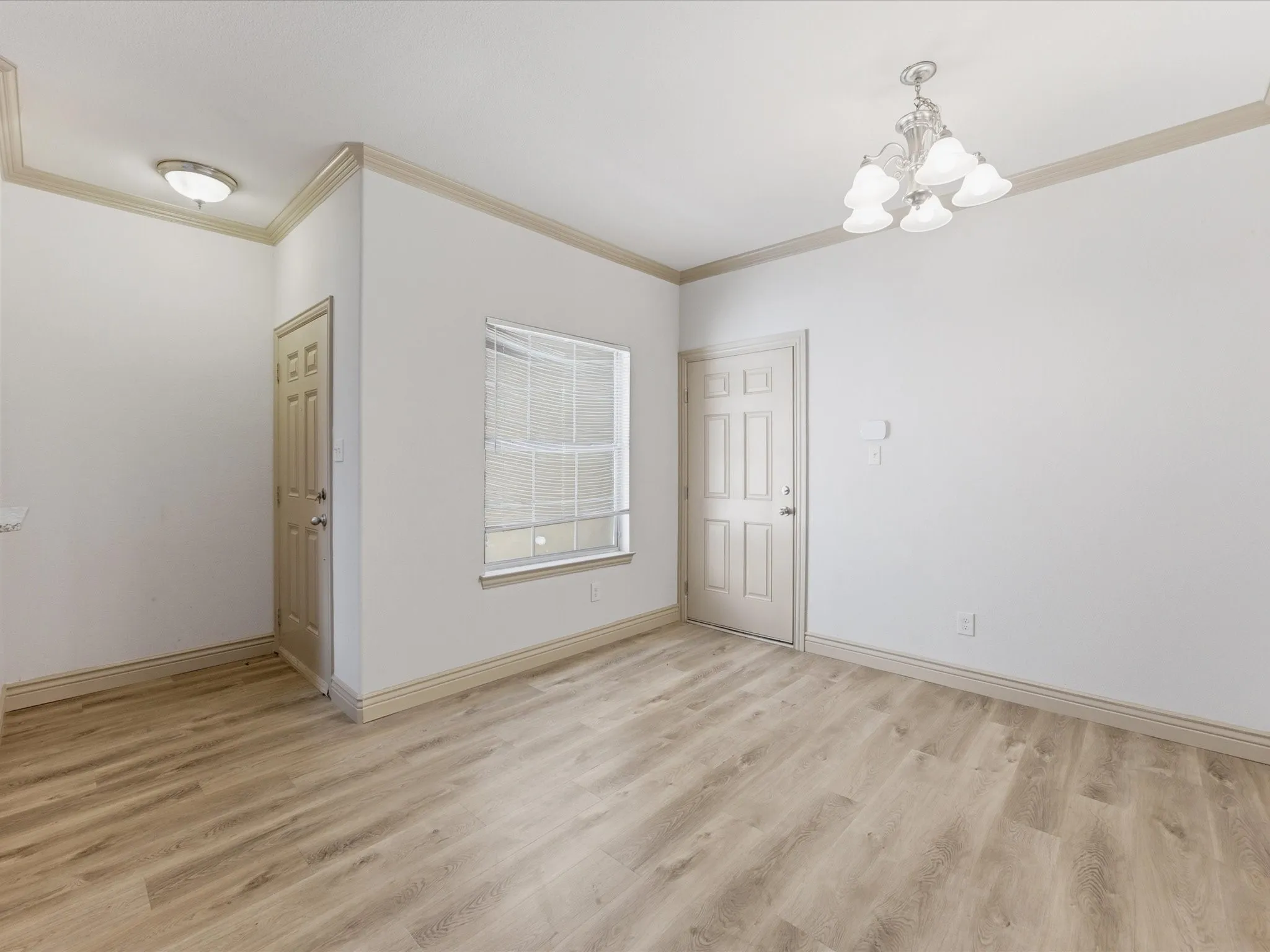 Wood-finish flooring, crown molding, a window with blinds, a multi-paneled door, and a decorative chandelier