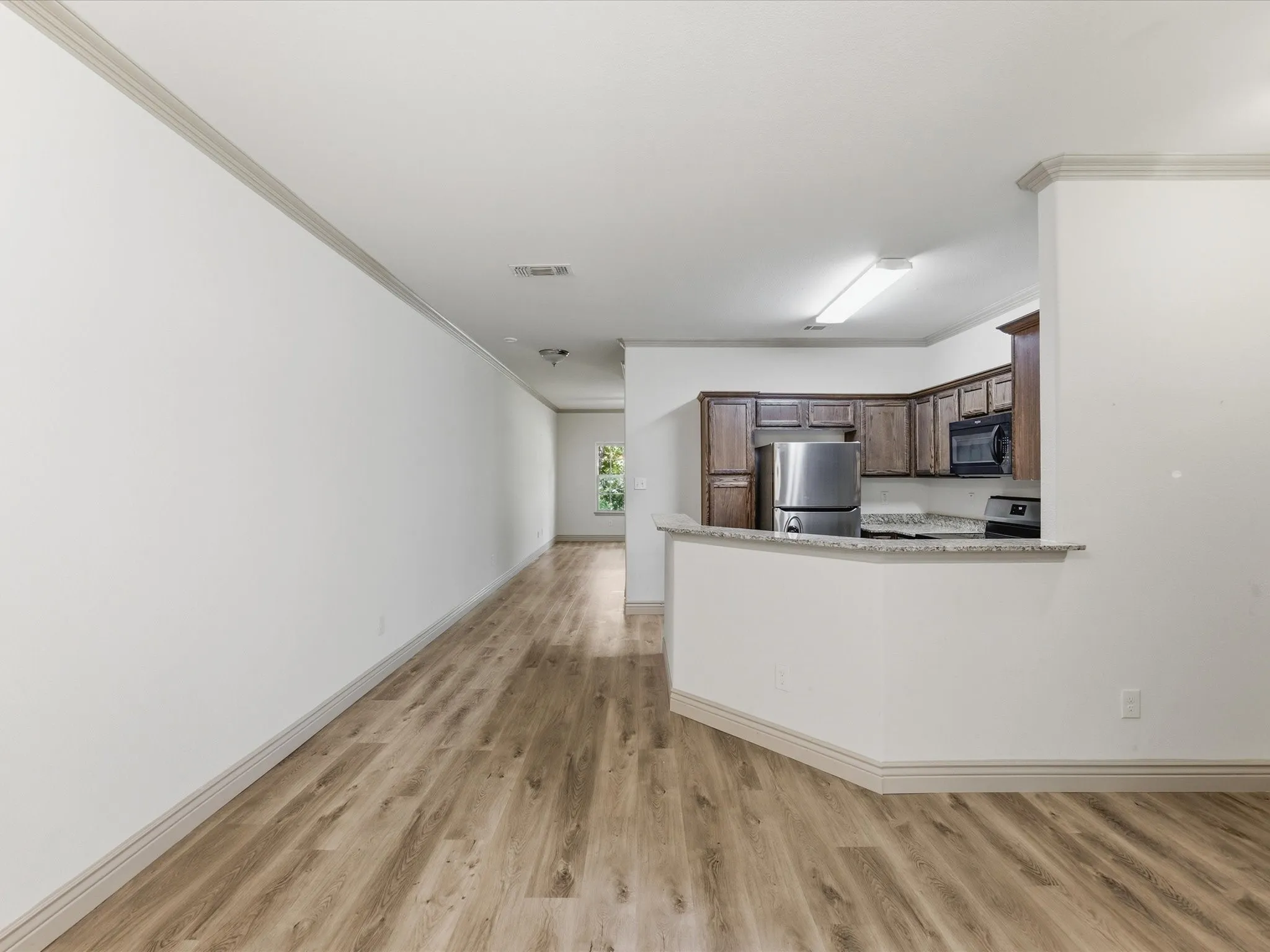 Wood-finish flooring throughout, crown molding, kitchen with dark wood cabinetry, stainless steel appliances, and a granite-style countertop