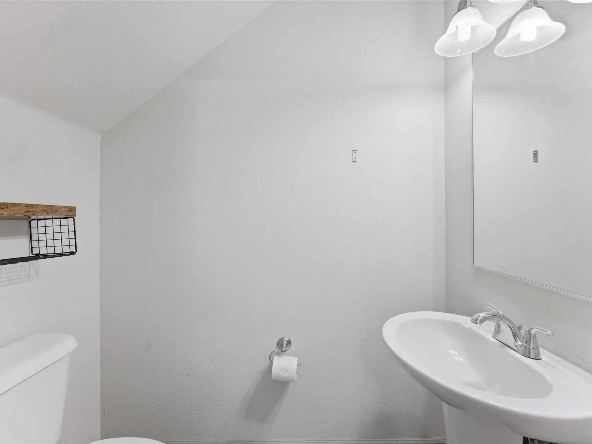 Pedestal sink with chrome faucet, wall-mounted mirror, and overhead lighting fixture