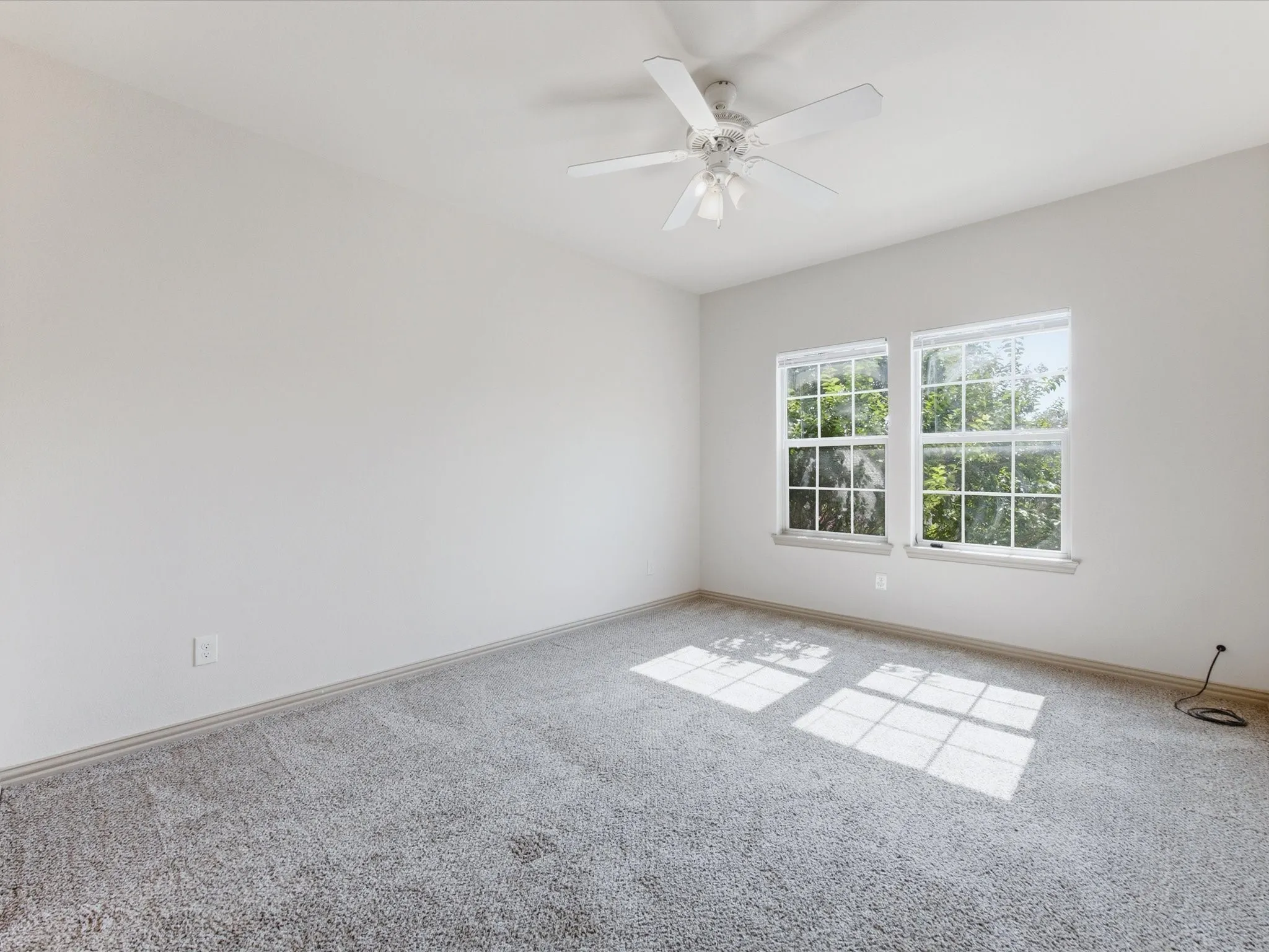 Light gray wall-to-wall carpeting with white walls, dual windows, and a ceiling fan with integrated lighting