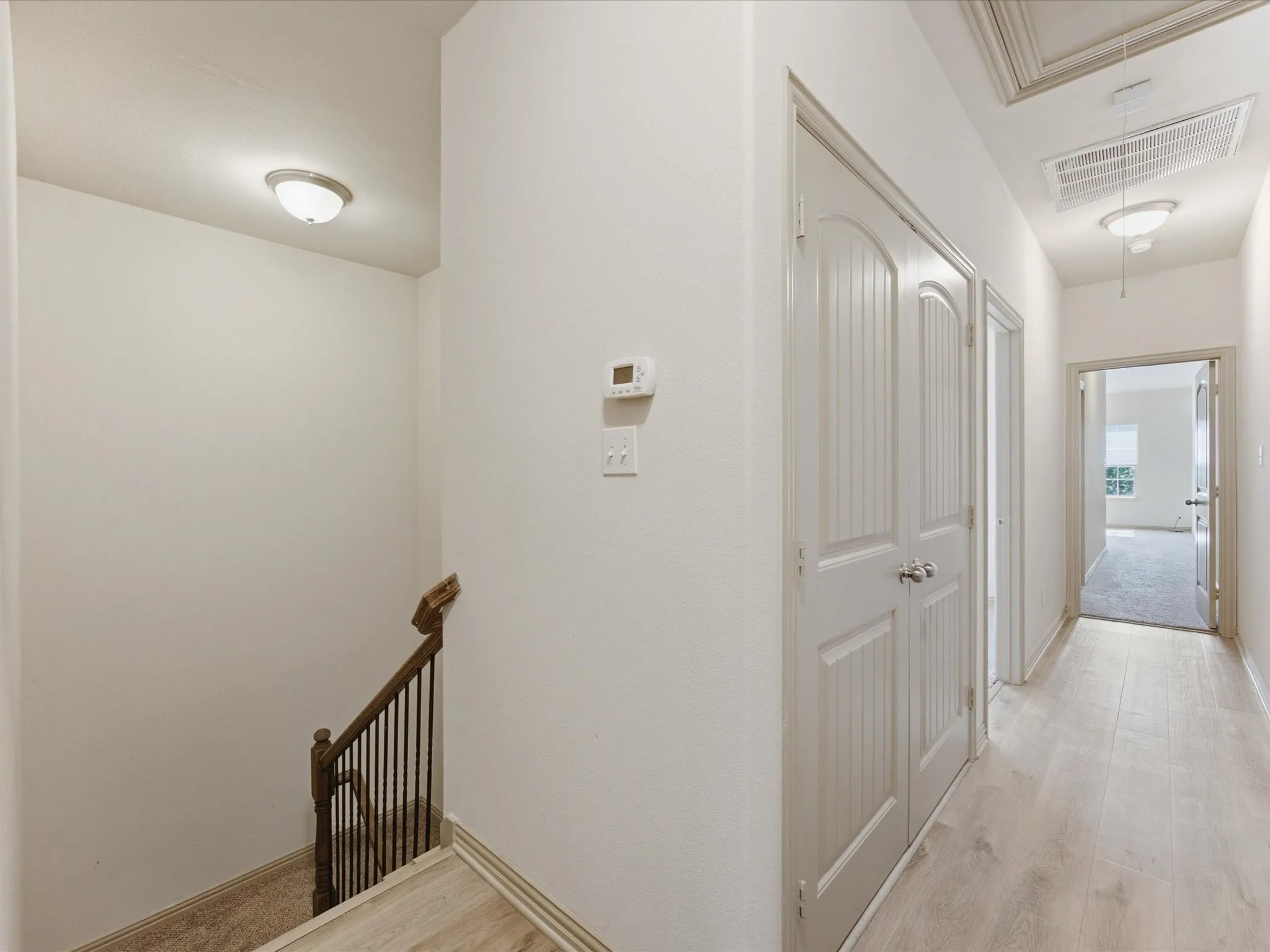 Wood-finish flooring, white paneled doors, recessed lighting, and a thermostat