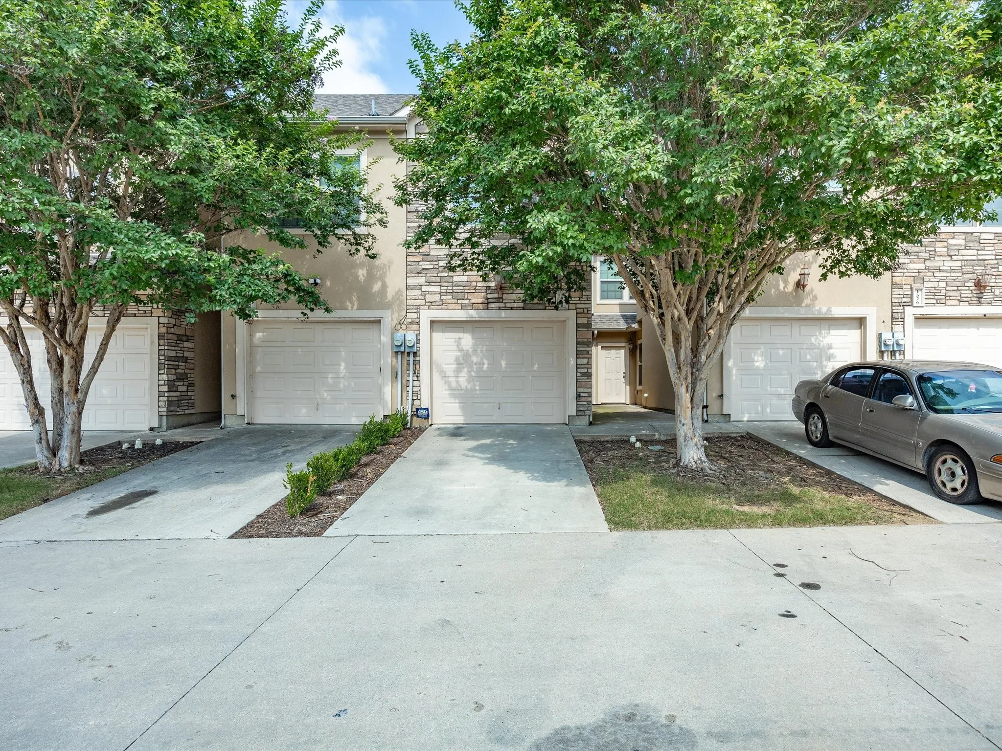 Stucco and stone exterior featuring multiple garage doors and established front landscaping