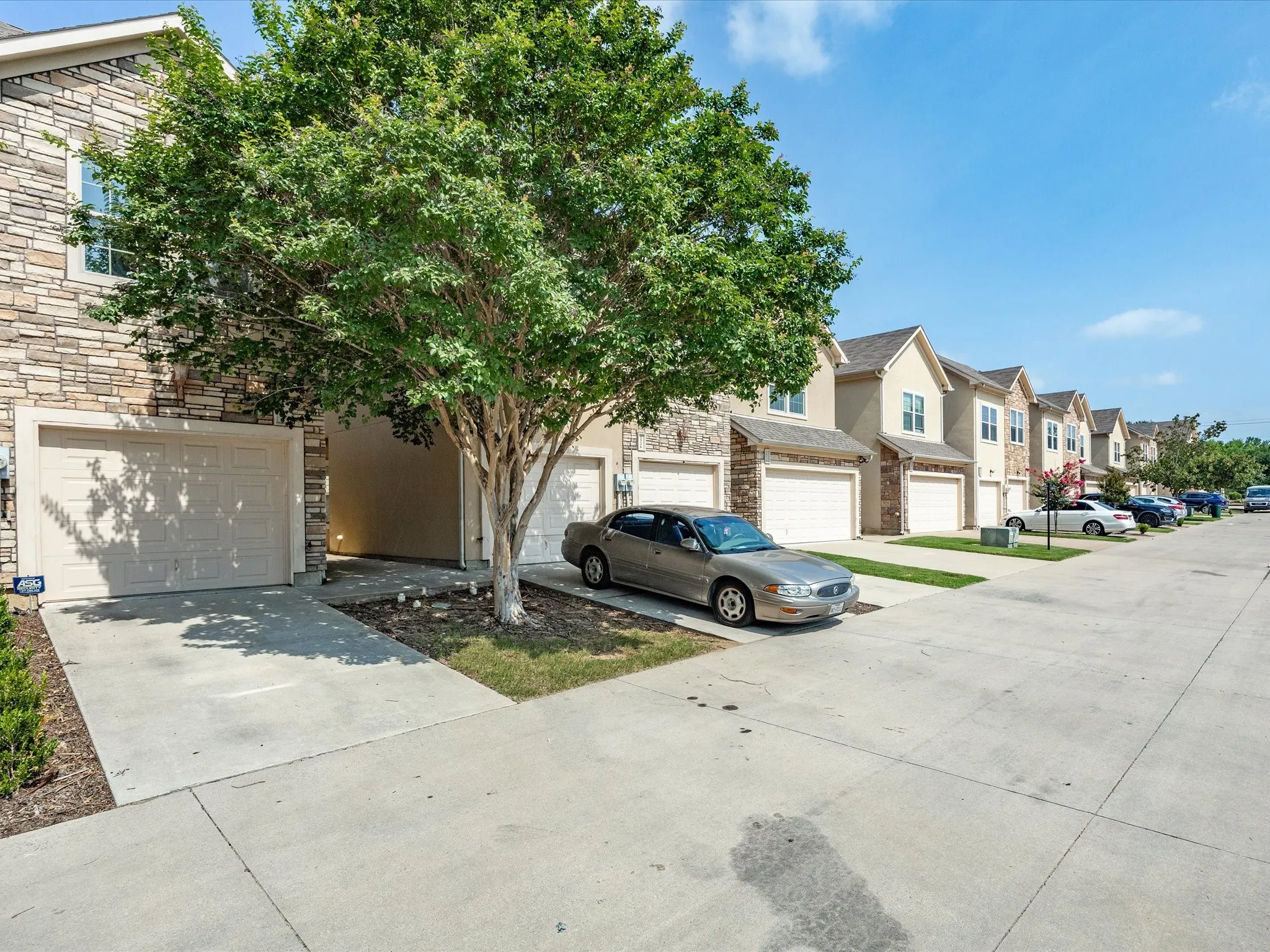 Stone veneer exterior, single-car garage, concrete driveway, mature tree, street-facing townhome