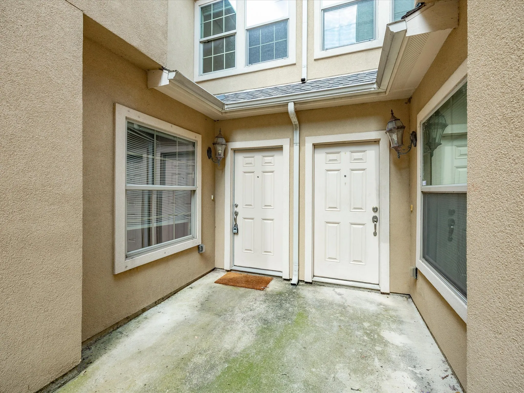 Stucco exterior with two paneled entry doors, two exterior wall sconces, and multiple window units