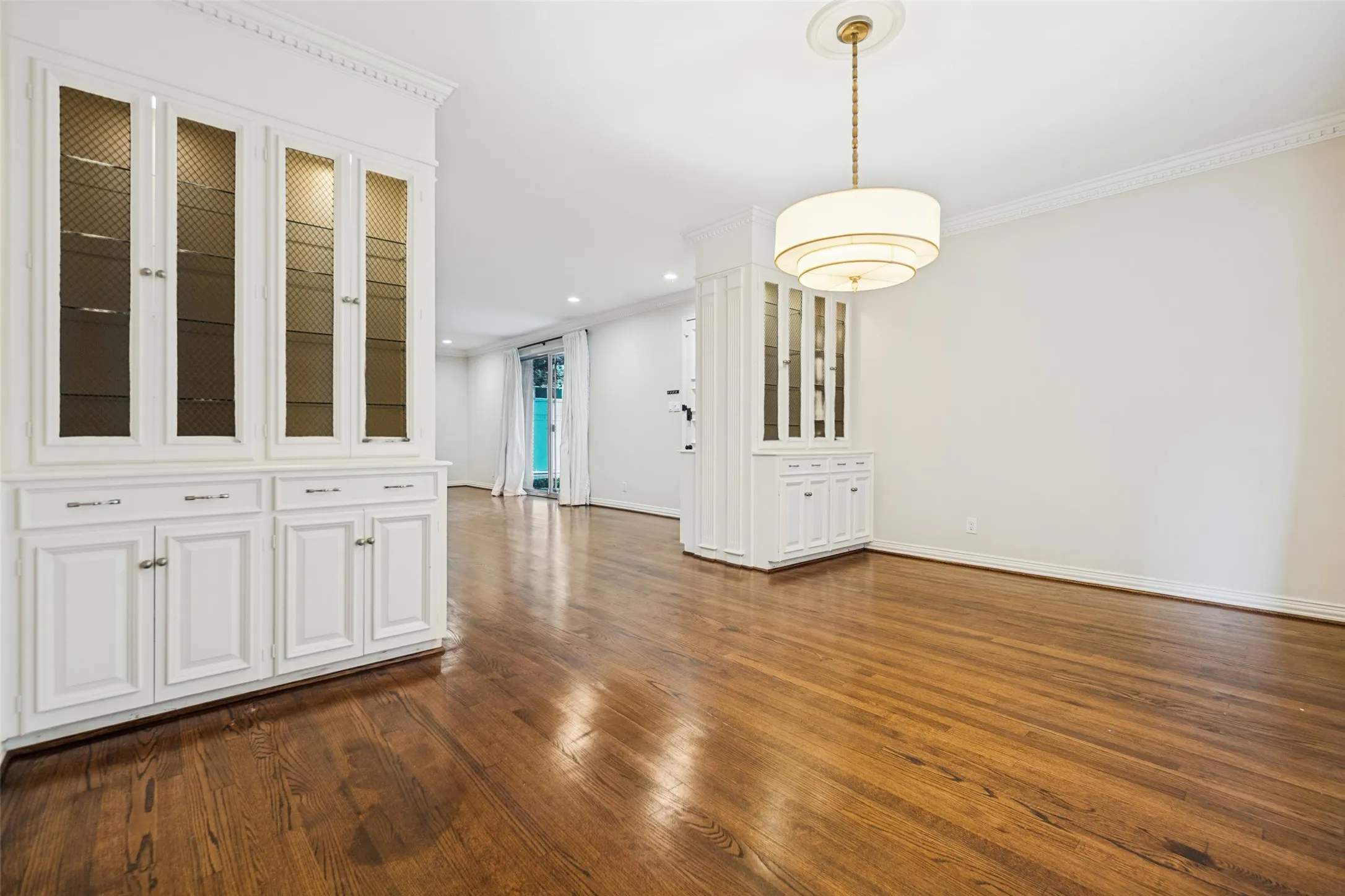 Hardwood flooring throughout, built-in cabinetry with glass-front uppers, crown molding, and a tiered drum chandelier