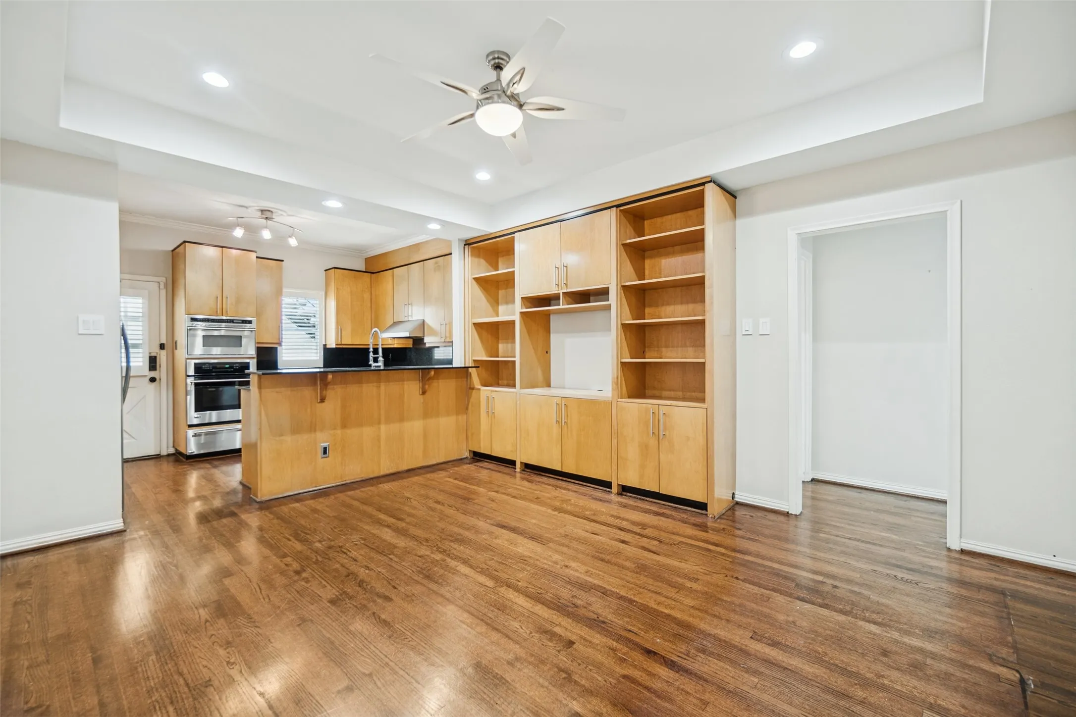 Wood-finish flooring, built-in shelving, recessed lighting, ceiling fan, and light wood cabinetry with stainless steel appliances