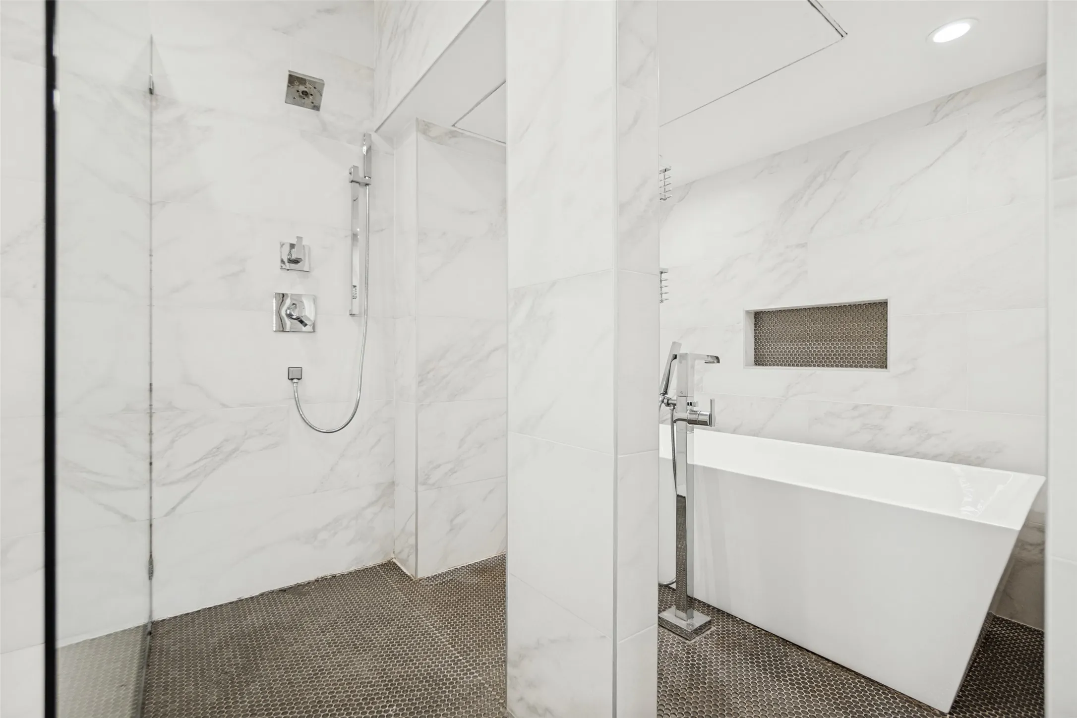 Wall-mounted shower system with a rain showerhead, freestanding soaking tub with floor-mounted faucet, full-height white tile walls, and dark tile flooring