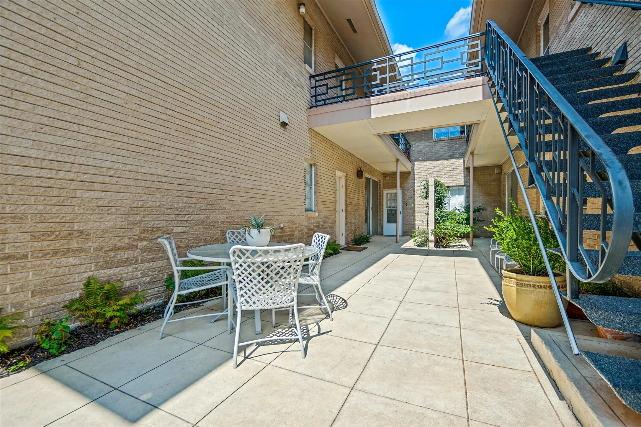 Tiled patio area with brick exterior, featuring an exterior staircase with metal railing, and a second-level balcony