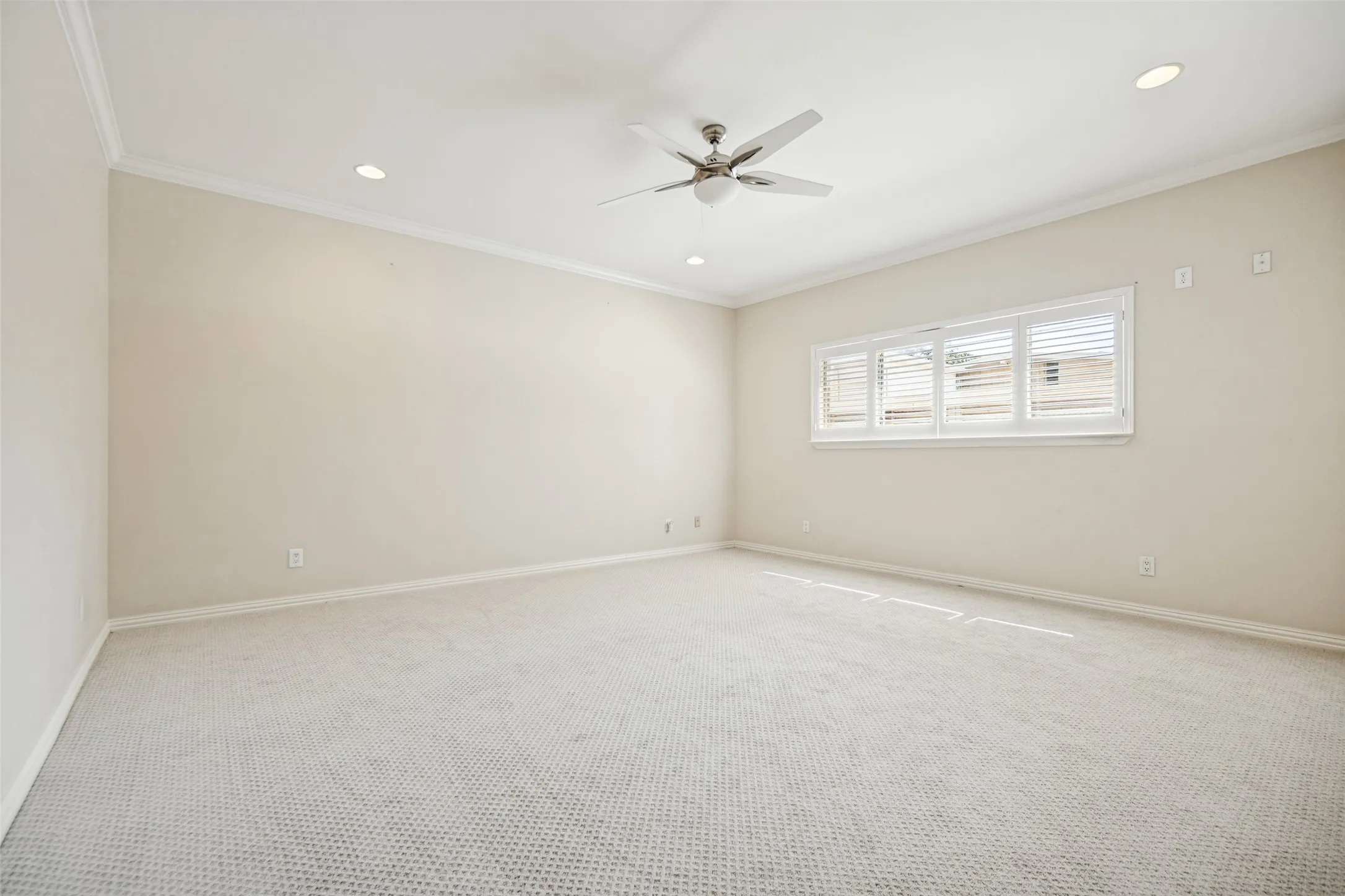 Recessed lighting complements a ceiling fan, crown molding, and carpet flooring