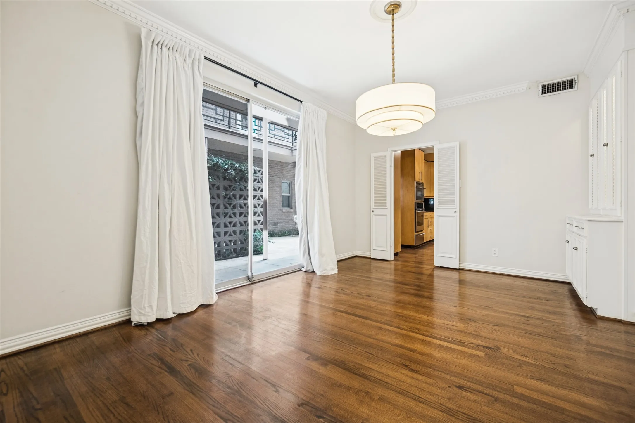 Hardwood flooring, crown molding, double bifold doors, built-in cabinetry, and a tiered drum chandelier