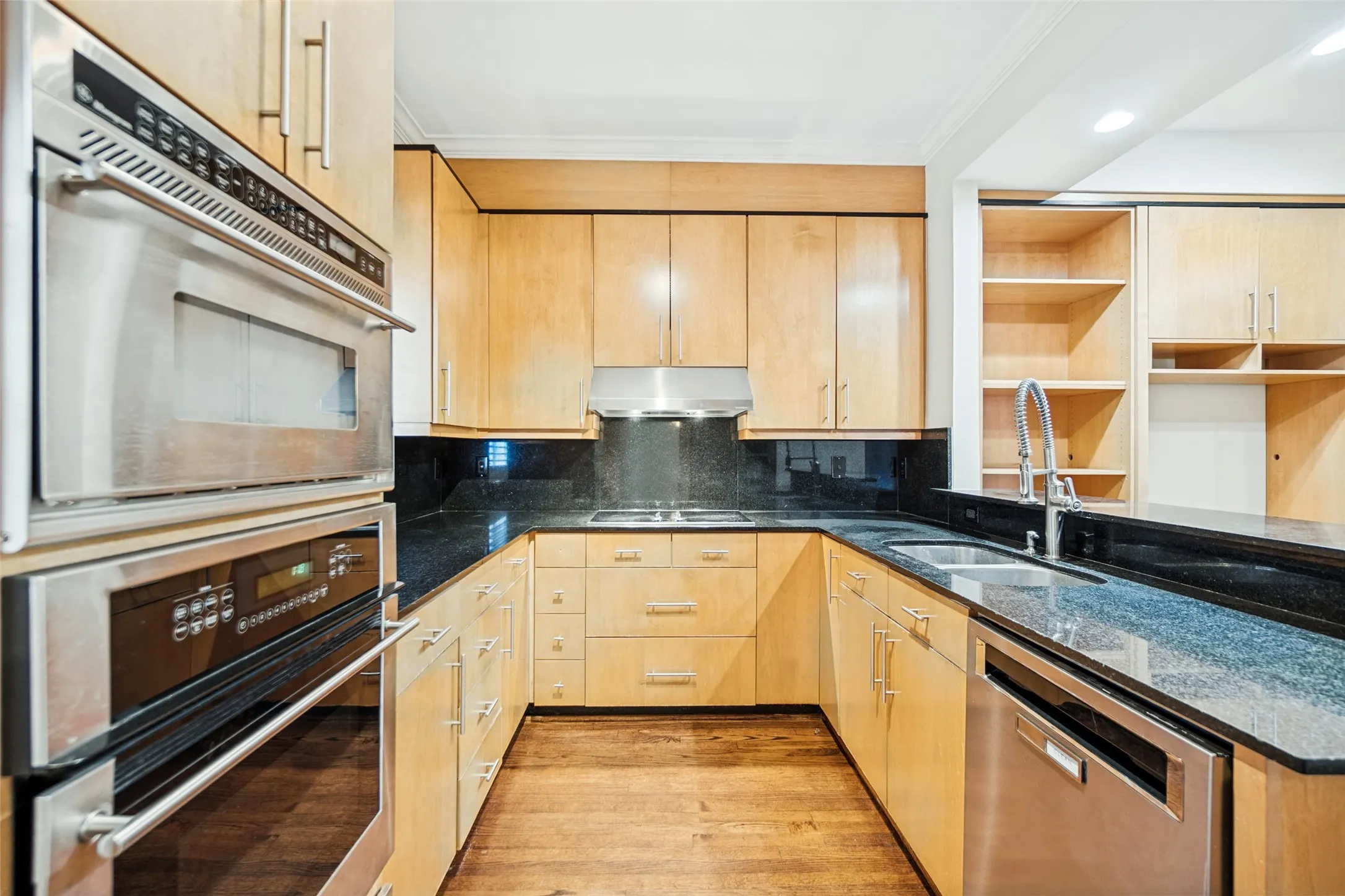 U-shaped kitchen featuring wood cabinetry, stainless steel appliances, dark stone countertops, and wood-finish flooring