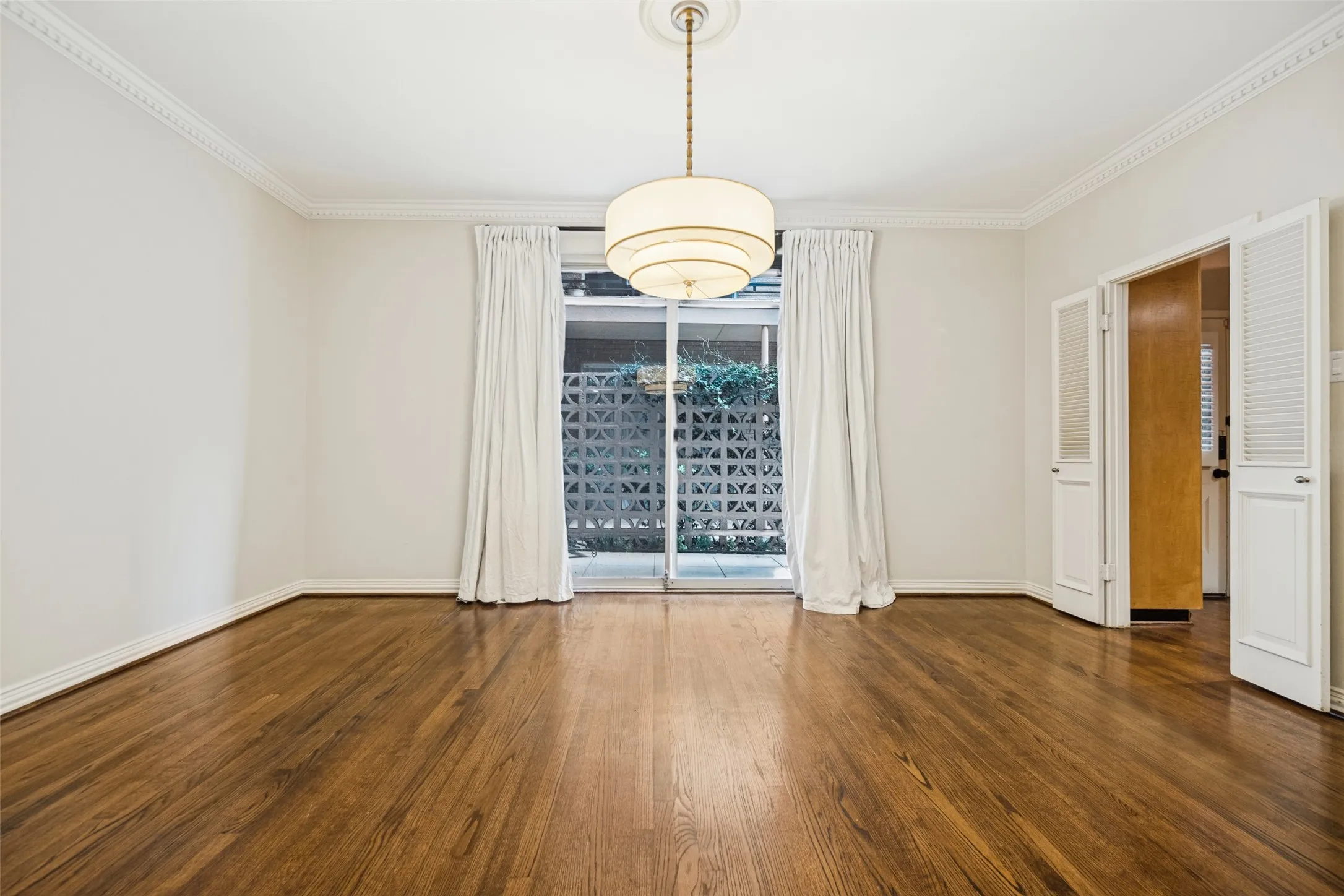 Hardwood flooring, crown molding, white trim, sliding glass door, and a decorative pendant light fixture