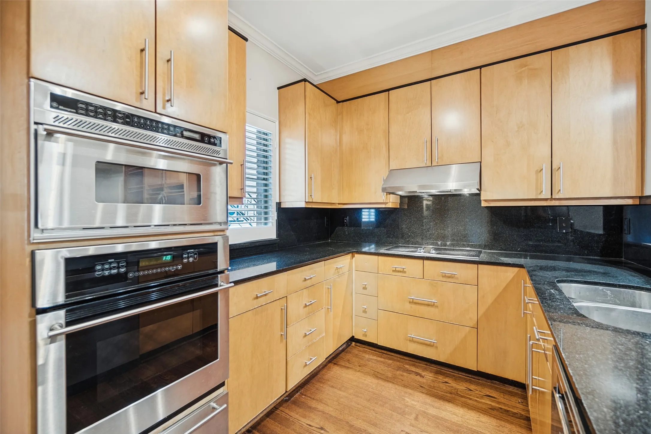 Kitchen featuring wood-finish cabinetry, stainless steel appliances, dark countertops, and a dual basin sink