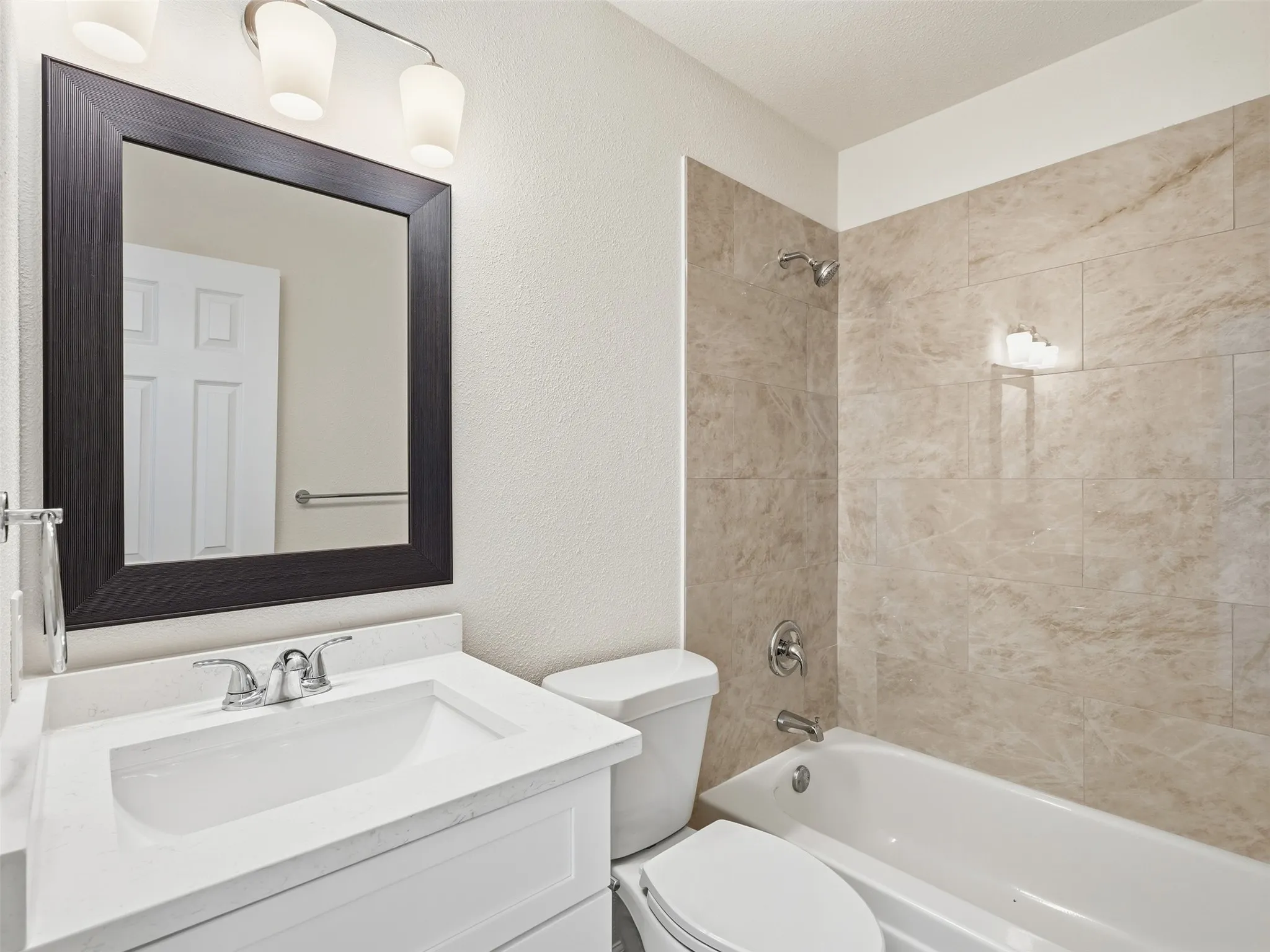Bathroom with a vanity, integrated sink, framed mirror, and a bathtub with tiled surround