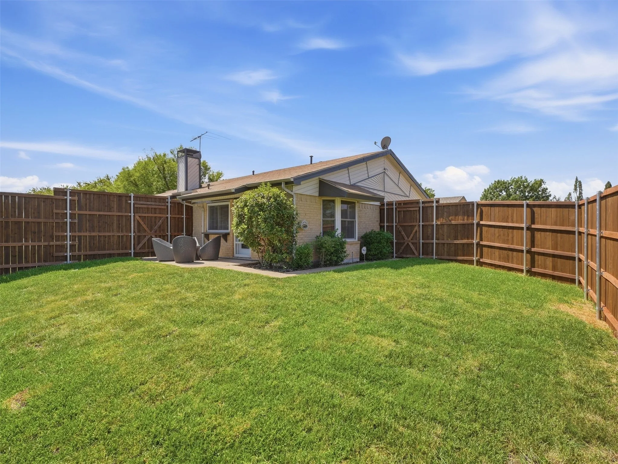 Manicured lawn with a privacy fence, a concrete patio, and a brick chimney