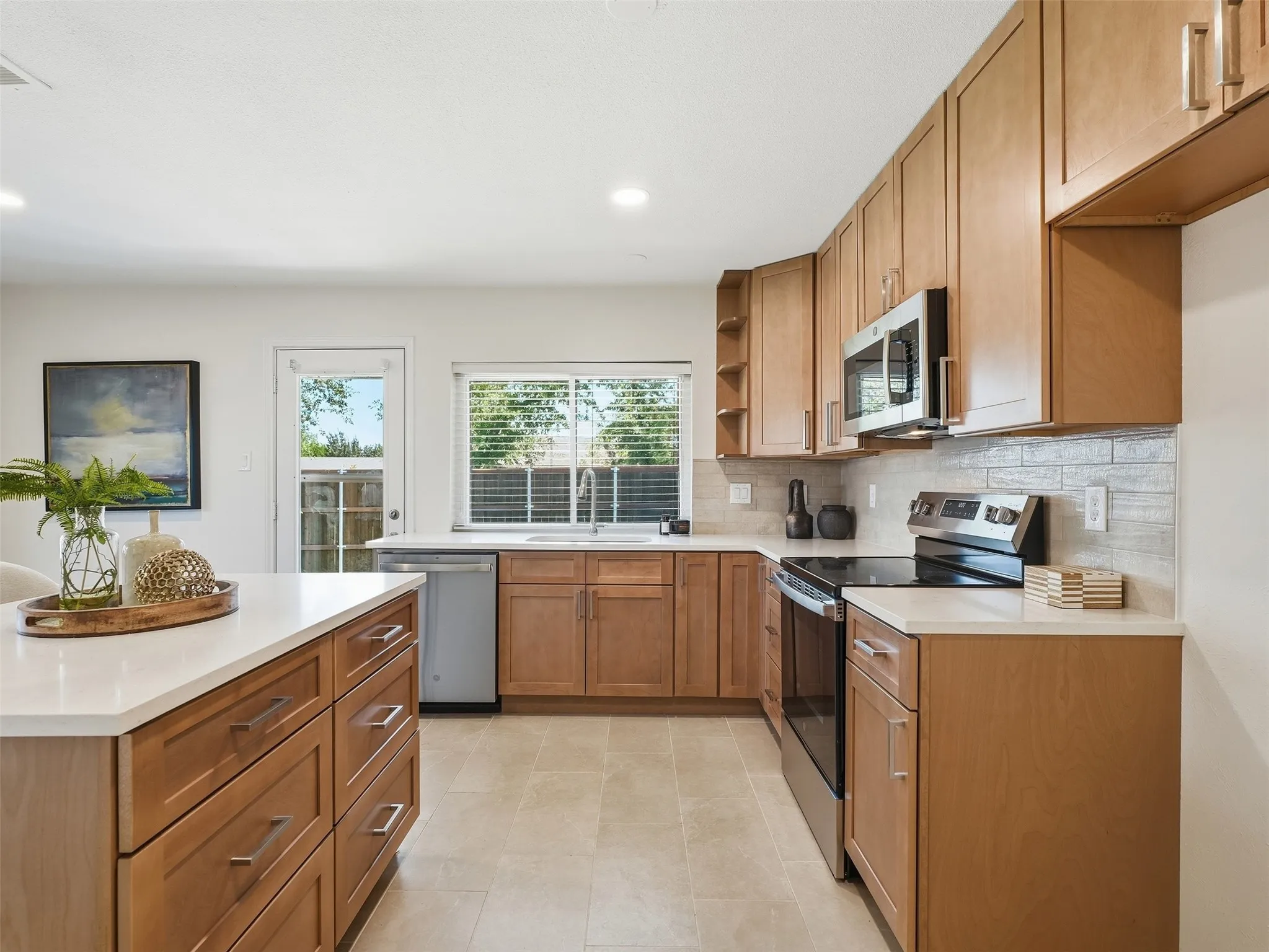 Kitchen featuring abundant wood cabinetry, light-toned countertops, stainless steel appliances, and a tiled backsplash