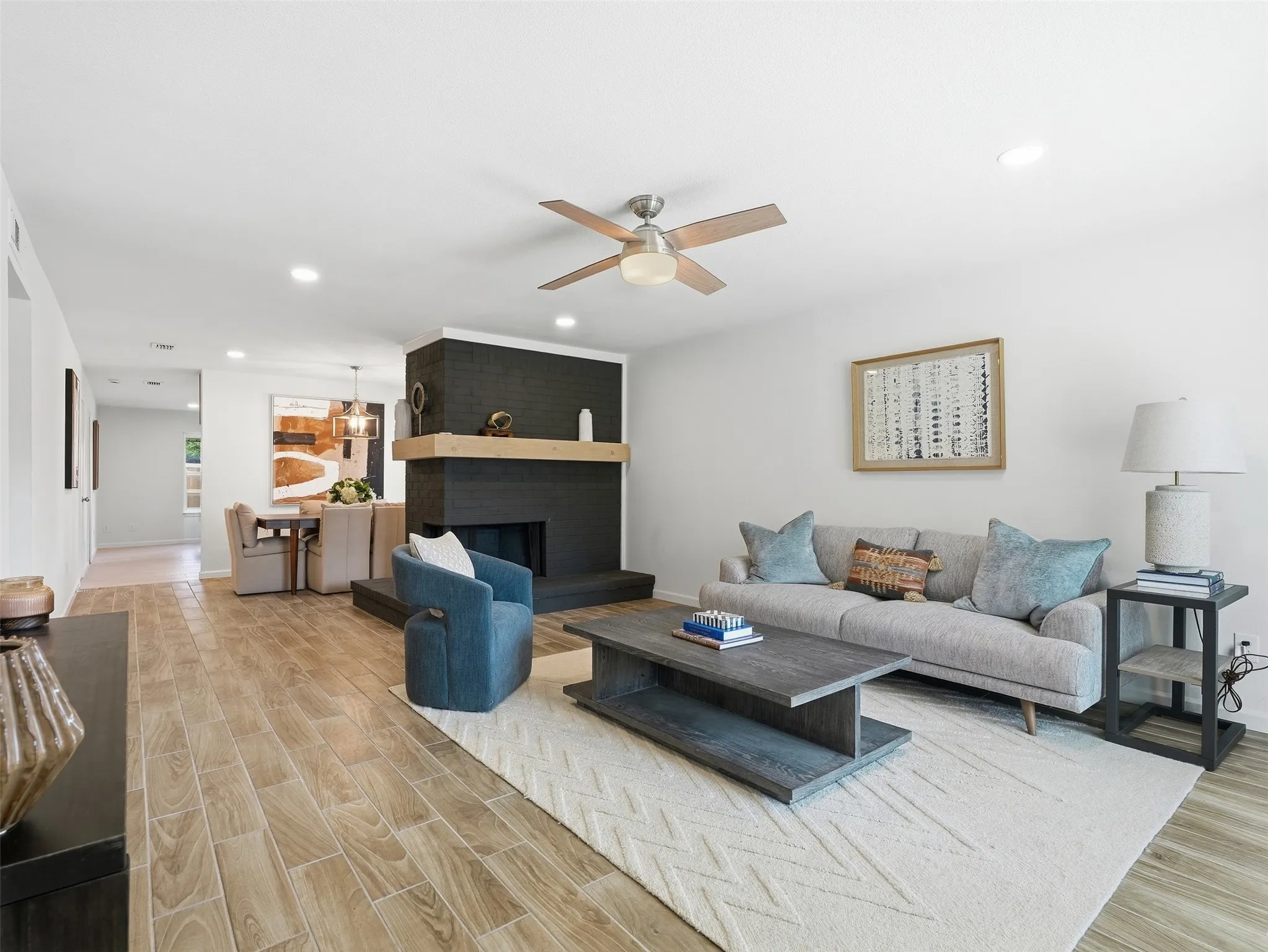 Living area featuring wood-finish flooring, a contemporary fireplace with a dark tile surround and a light wood mantel, and a ceiling fan
