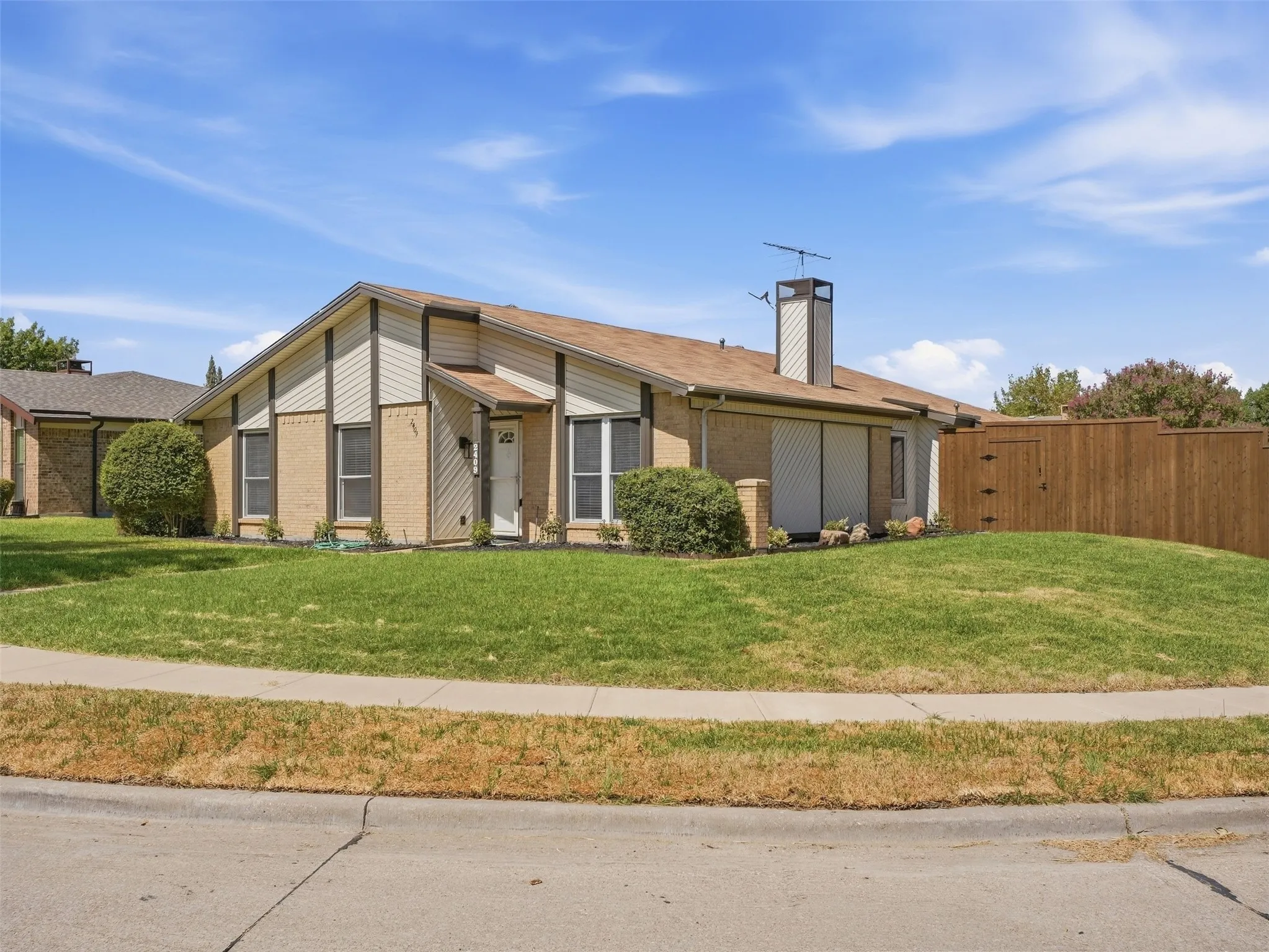 Brick and siding exterior with a peaked roofline, front entry, and a wooden privacy fence