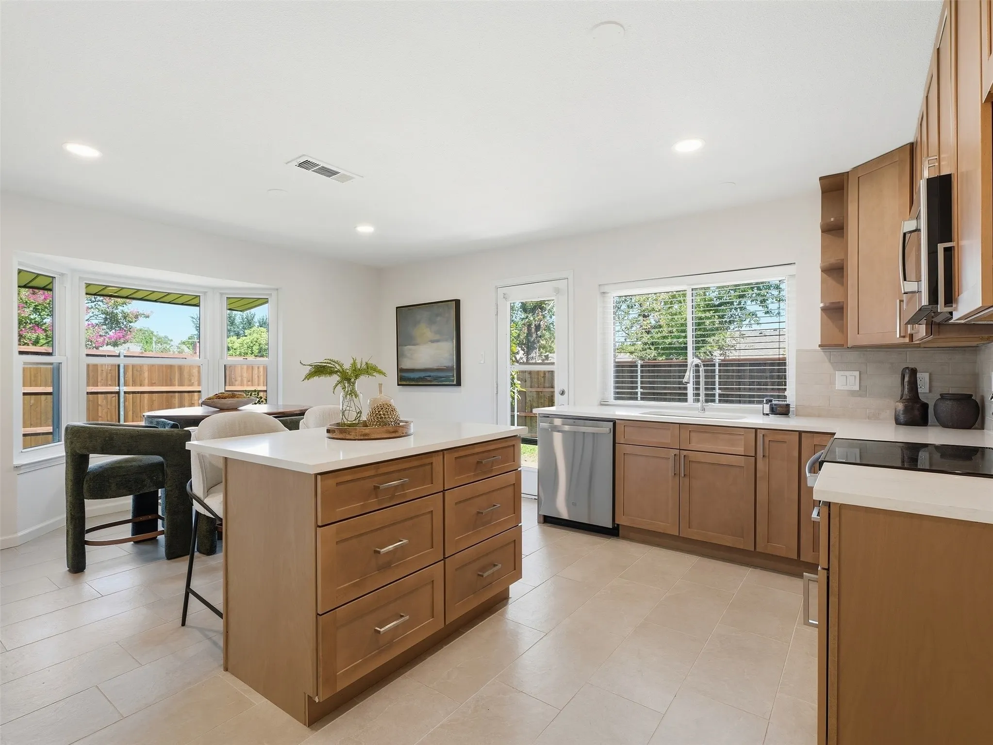 Kitchen featuring a center island with storage, light wood cabinetry, white countertops, stainless steel appliances, and tile flooring