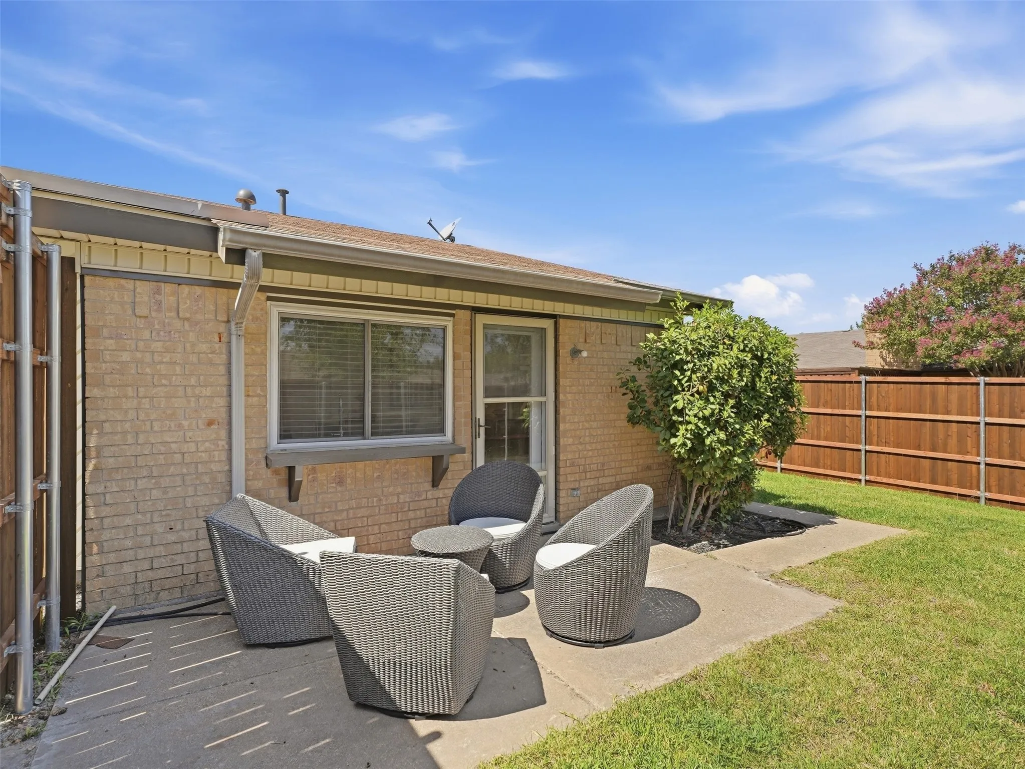 Brick exterior with an expansive concrete patio, established landscaping, and a wooden privacy fence