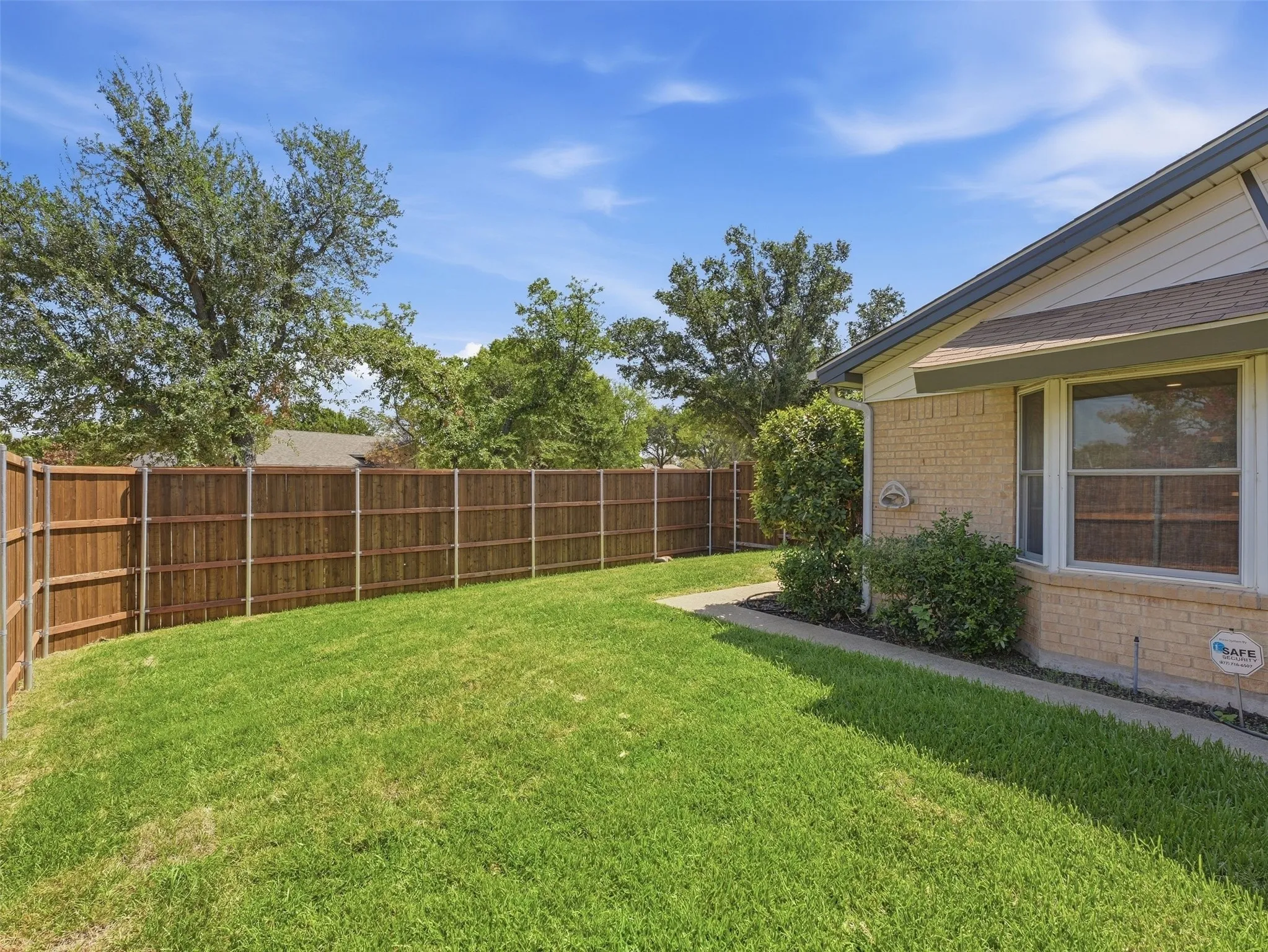 Expansive fenced backyard featuring a manicured lawn, established privacy fence, and mature trees