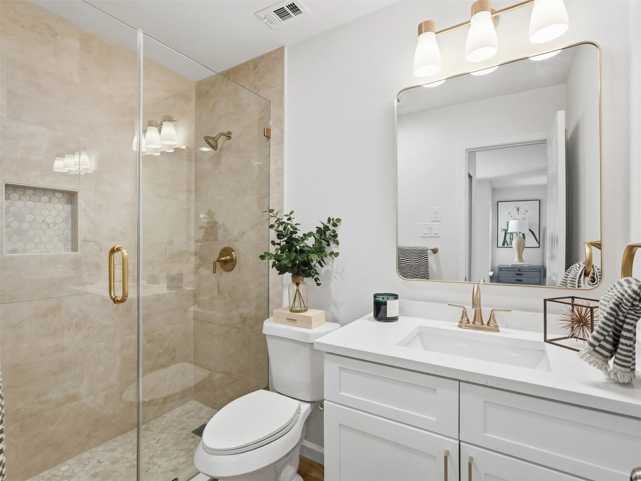 Frameless glass shower enclosure with brass hardware, a built-in shower niche, and mosaic tile flooring