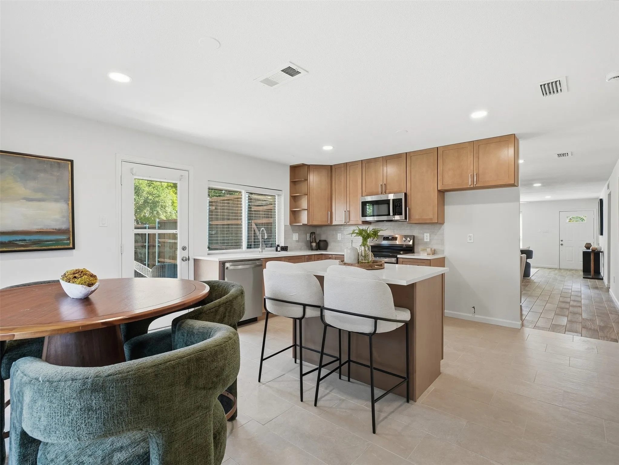 Contemporary kitchen featuring light wood-finish cabinetry, stainless steel appliances, a center island with countertop seating, and light-toned tile flooring