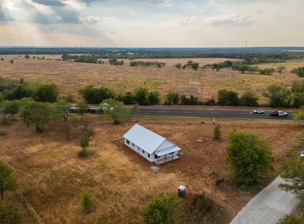 White-sided building with a metal roof, located on a large parcel of land with scattered trees