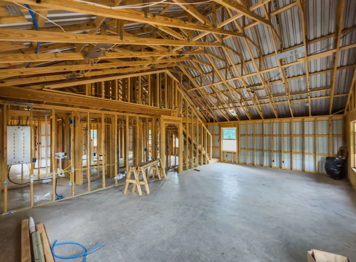Exposed wood framing, vaulted ceiling, concrete flooring, interior wall framing, and visible electrical conduit