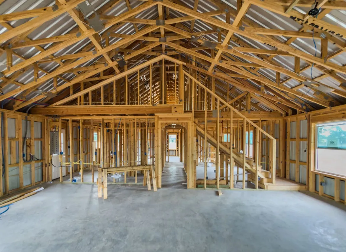 Expansive interior framing with visible wood trusses and a concrete slab foundation