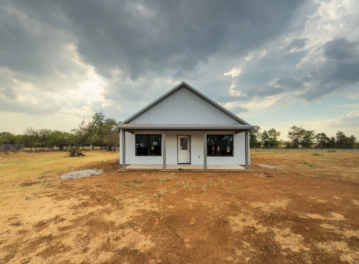 Gable roofline, white vertical siding, covered front porch, black-framed windows, and a single entry door